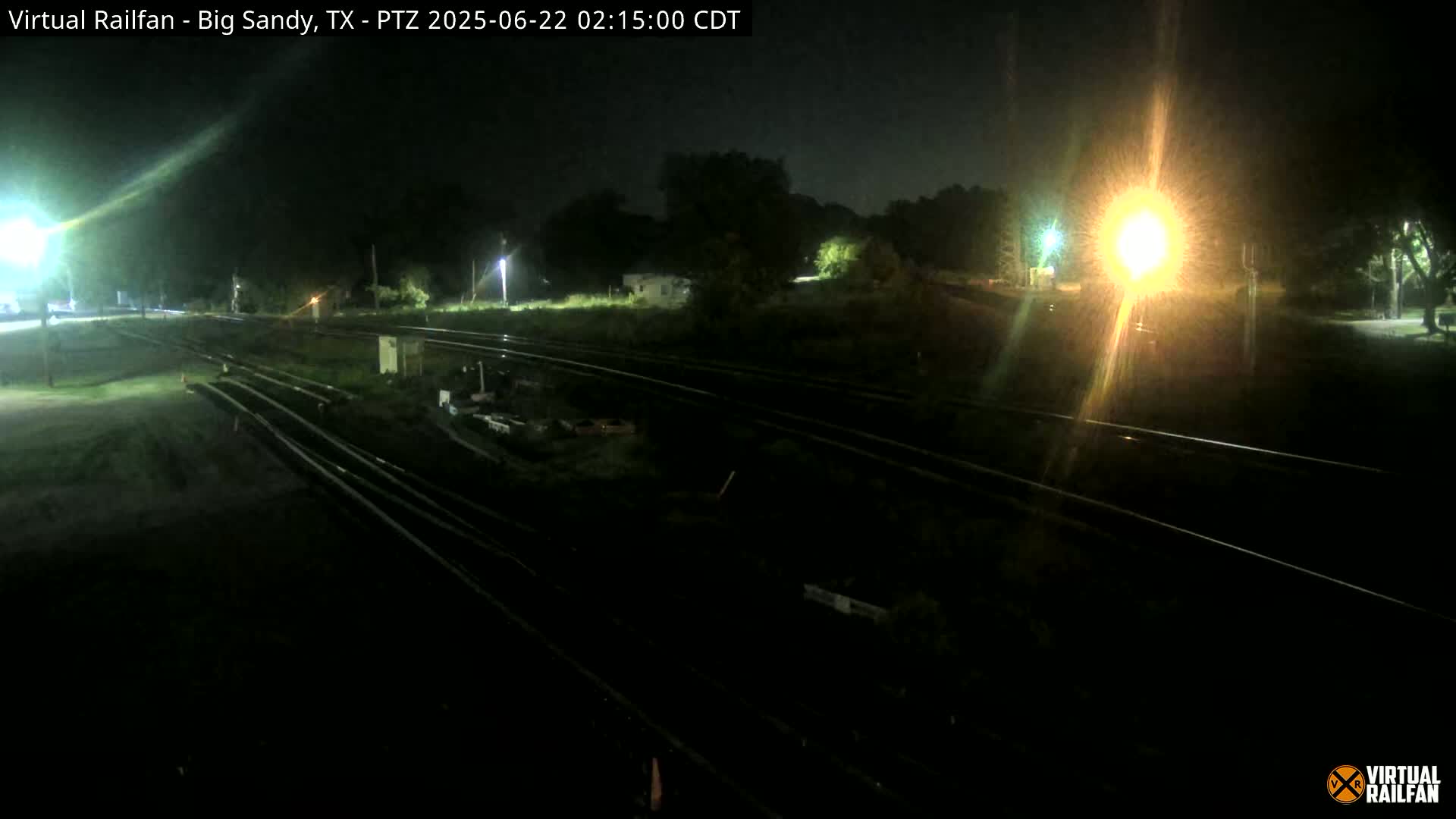 A nighttime view of several sets of train tracks in a dark, grassy area, illuminated by artificial lights.