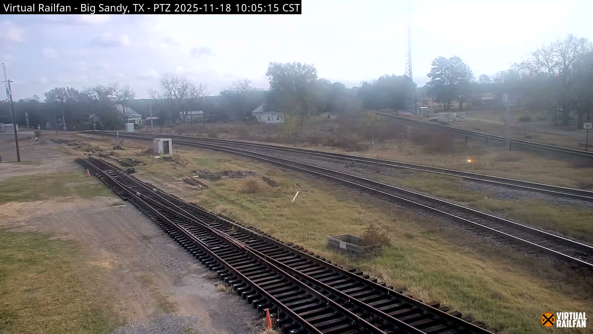 At night, several sets of train tracks are visible, illuminated by bright lights, with some vegetation and structures in the background.