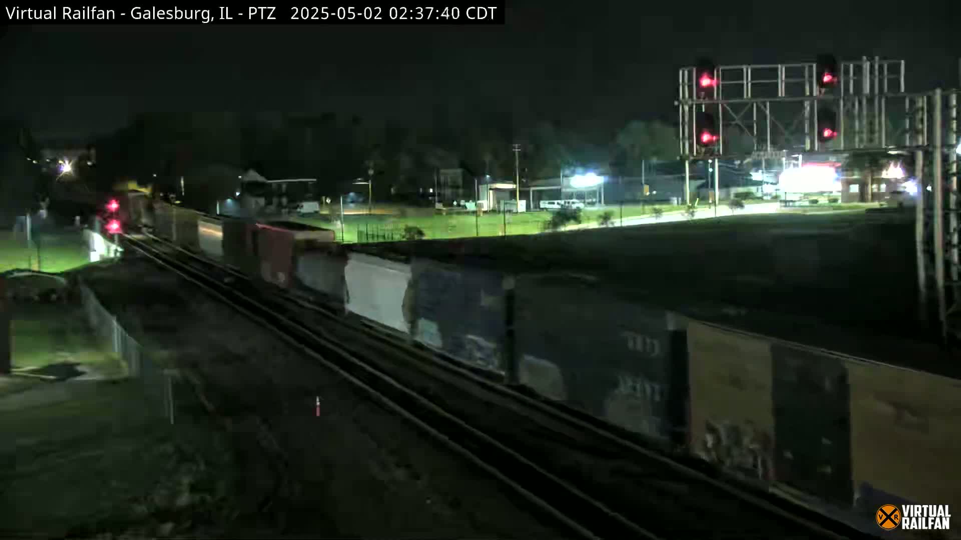 A long freight train passes under a red railroad signal at night.