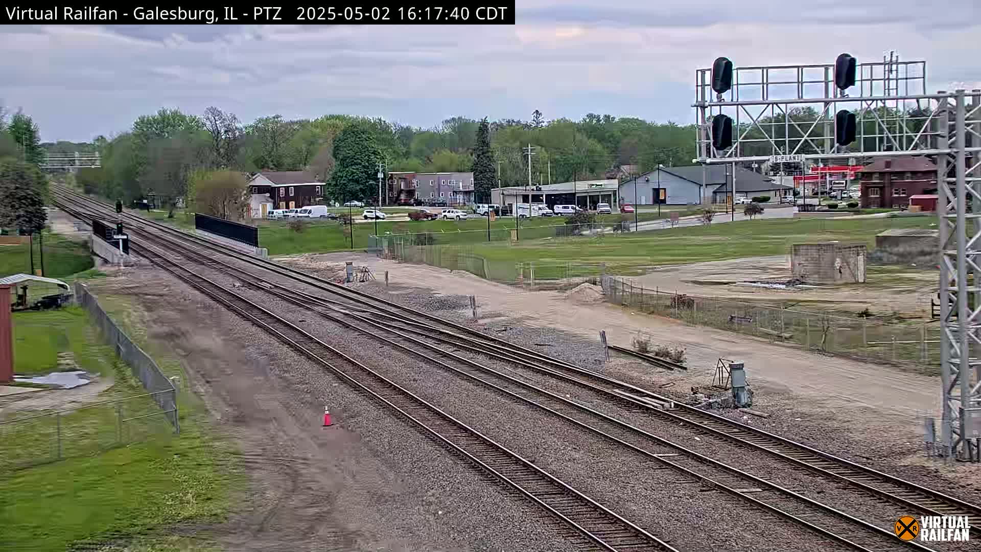 Multiple sets of train tracks extend into the distance under an overcast sky, passing by a town with buildings and a grassy area.