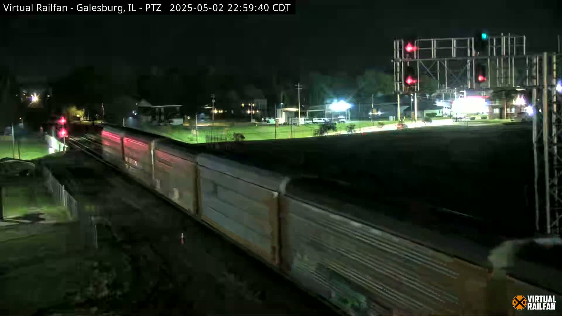 A long freight train passes under a railway crossing signal at night.