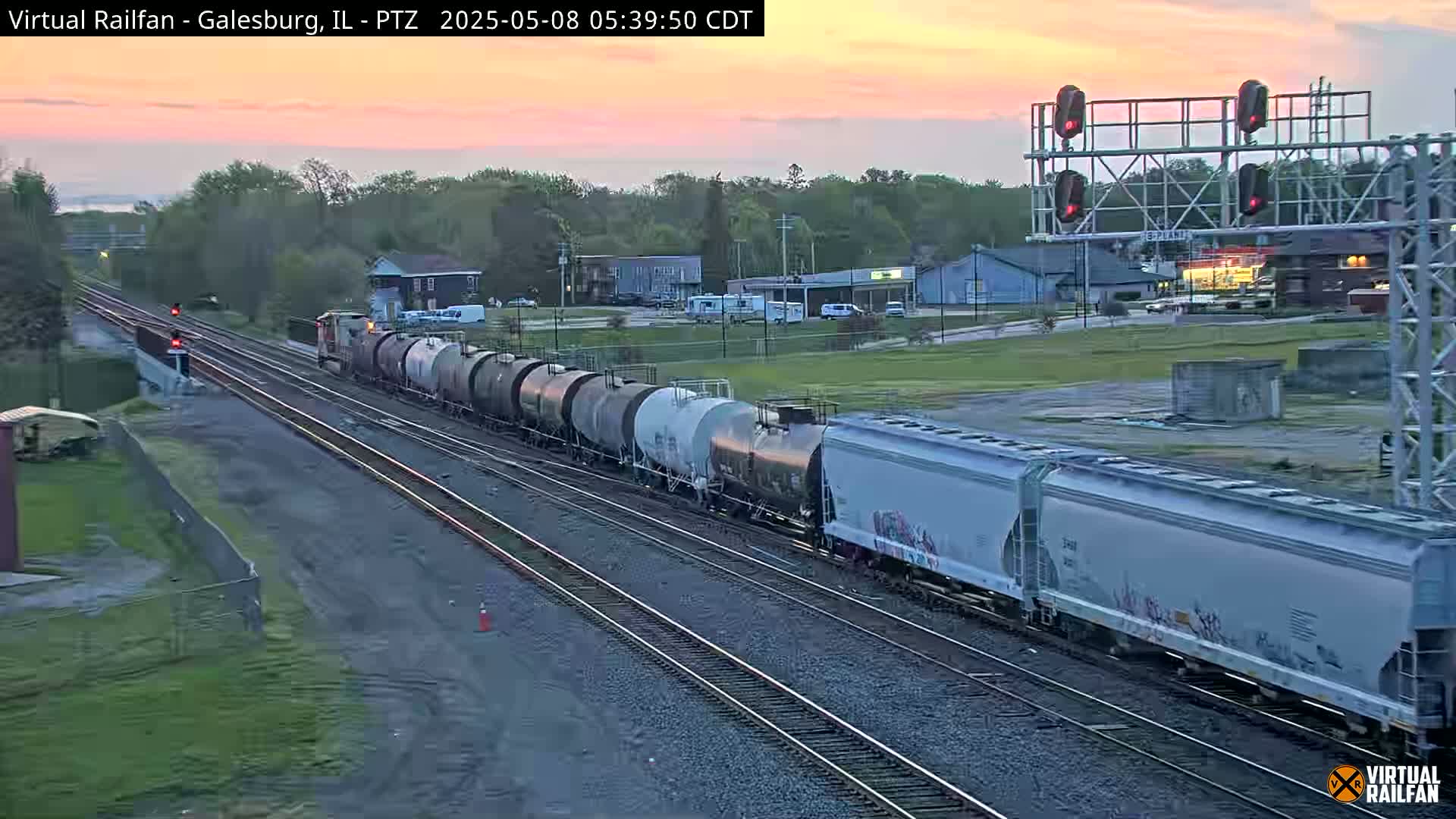 A long freight train passes under a railway crossing signal at sunrise.