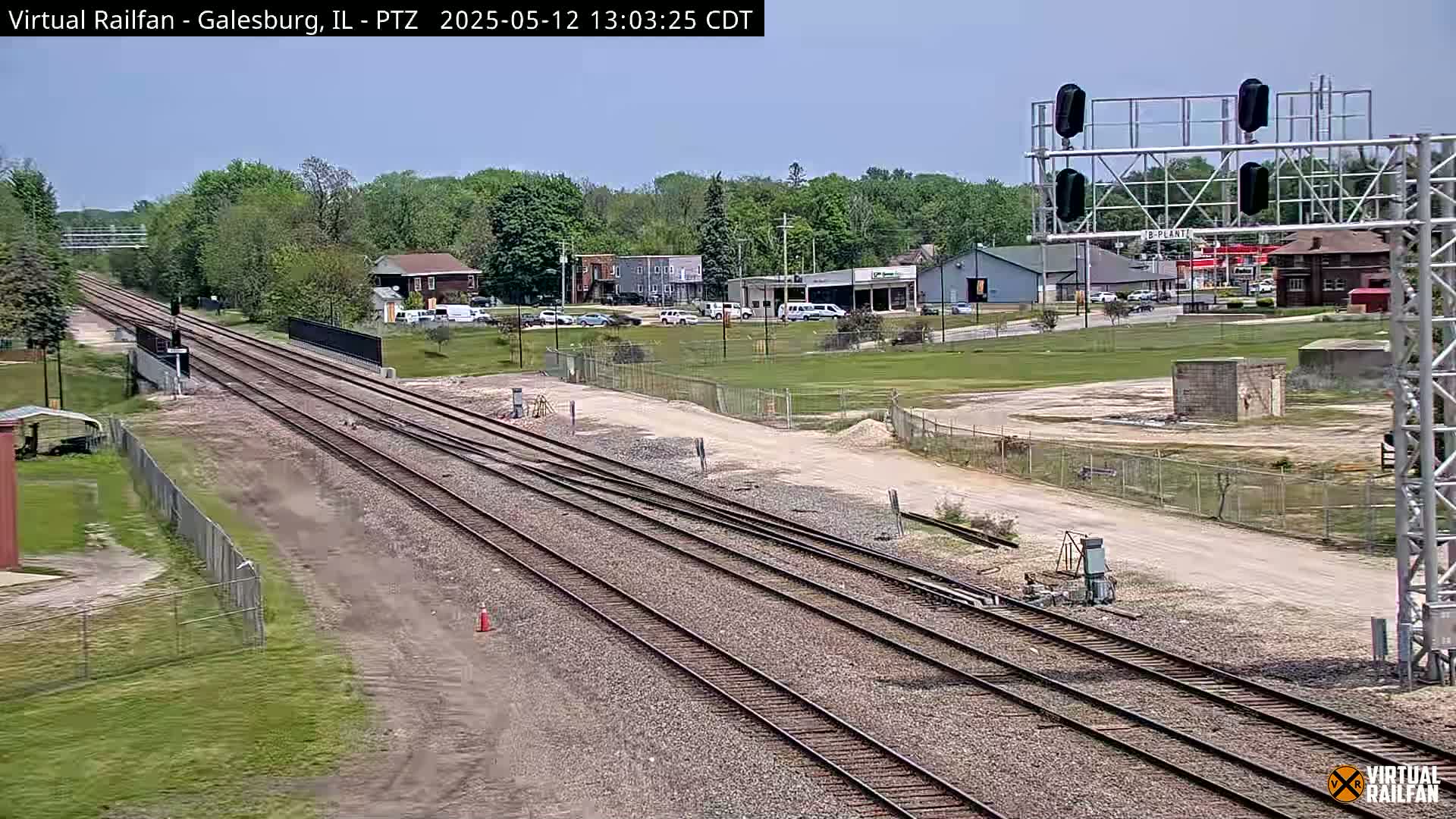 Multiple train tracks extend into the distance under a clear sky, past a small town with buildings and some parked cars.