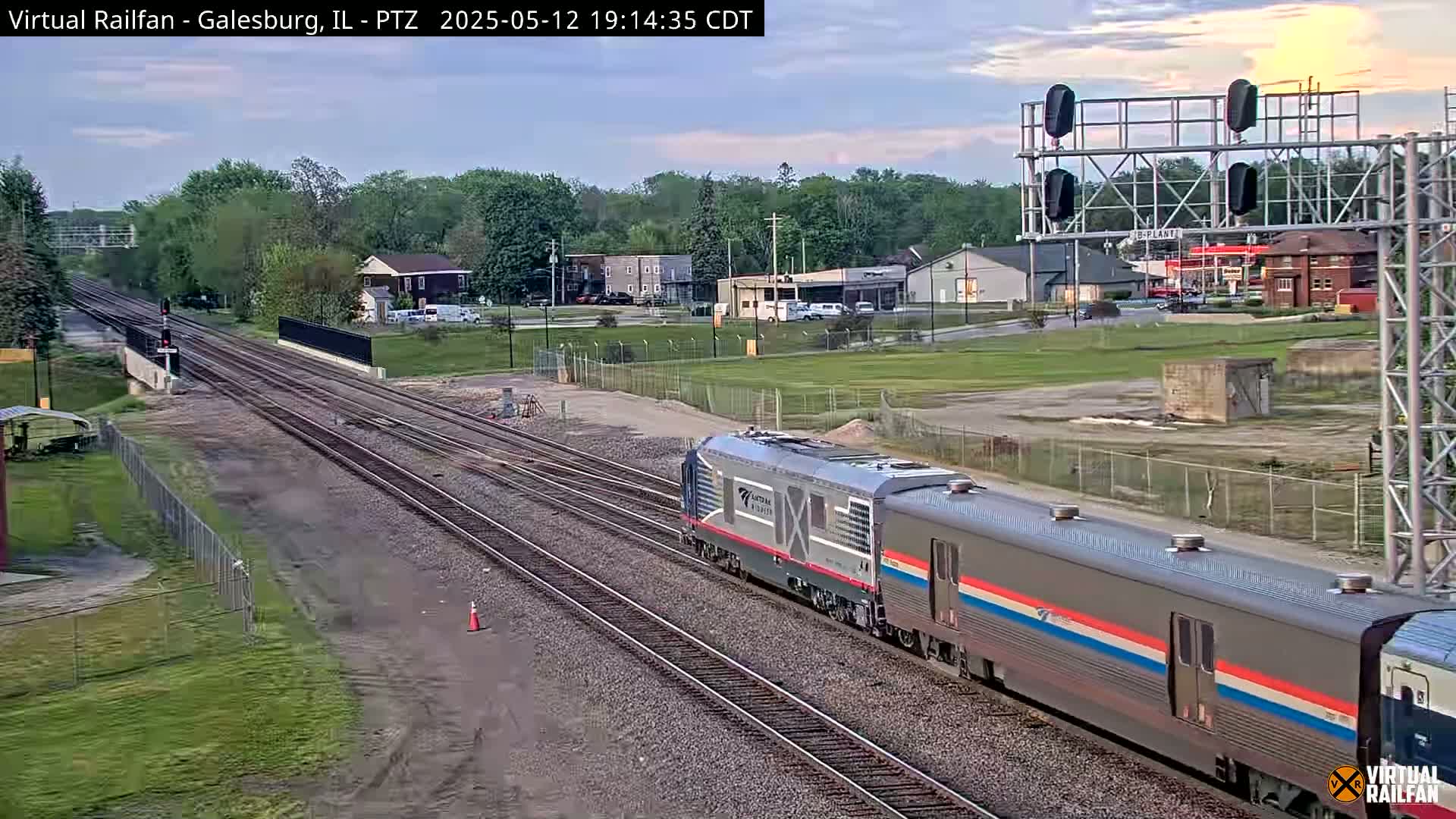A long passenger train passes by on a railway track under a partly cloudy evening sky.