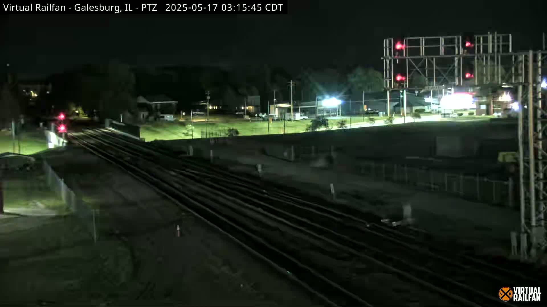 A nighttime view of multiple train tracks intersecting at a railroad crossing, with red signal lights illuminated, under a clear, dark sky.