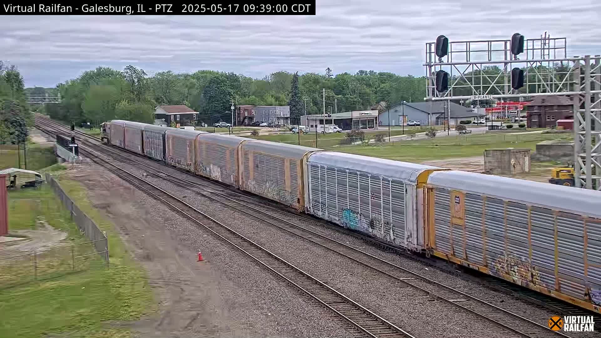 A long freight train passes through a small town on a partly cloudy day.