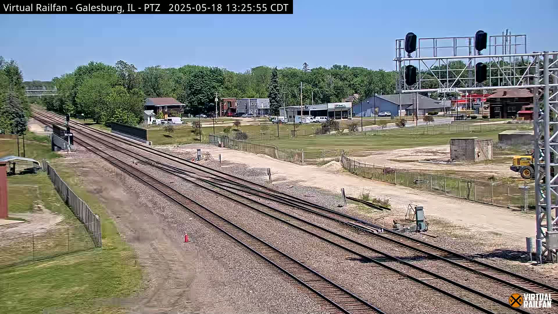 Multiple train tracks stretch into the distance under a clear, sunny sky, passing by a small town with buildings and a construction area.