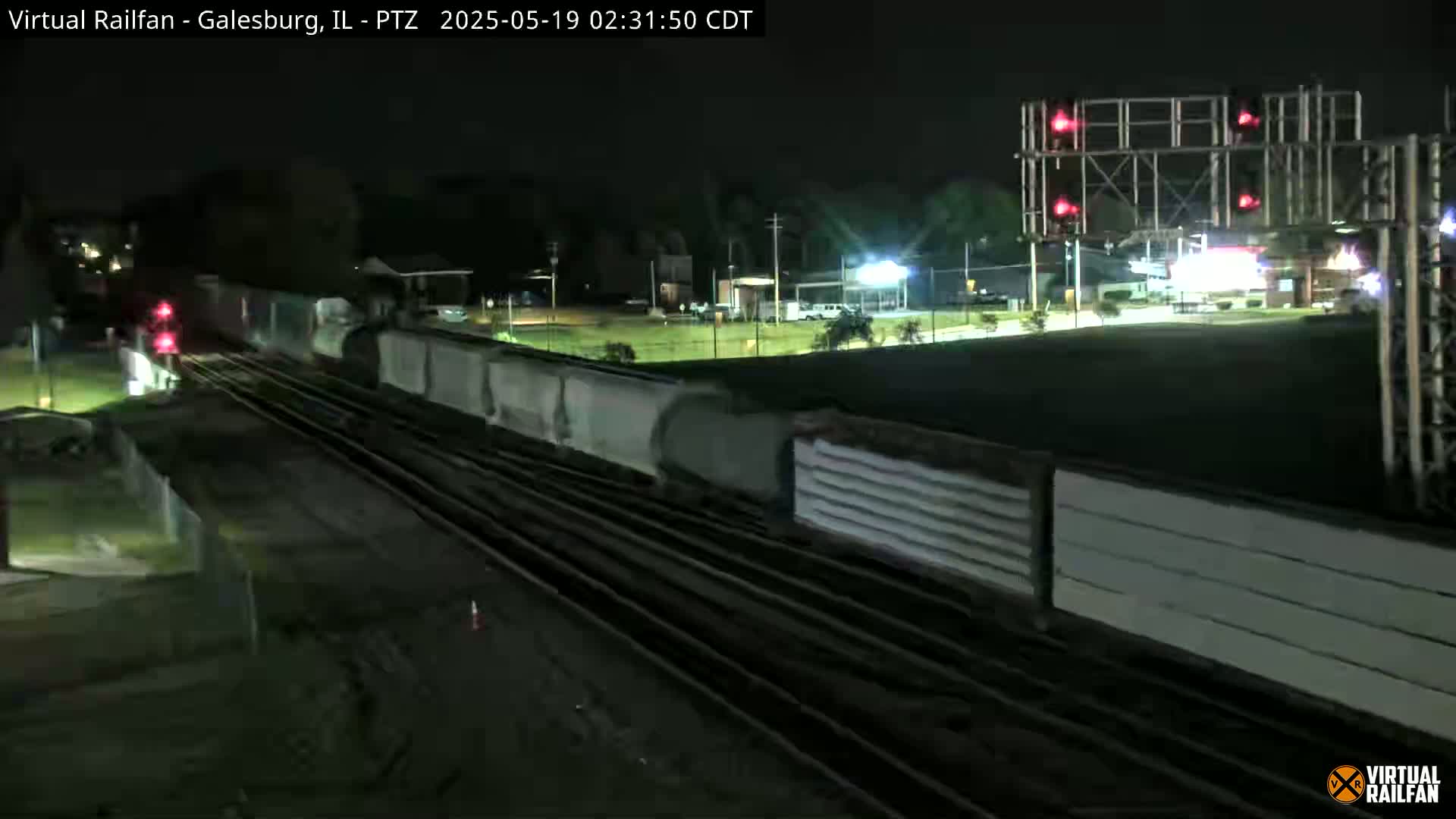 At night, a long freight train passes under a set of railroad crossing lights.
