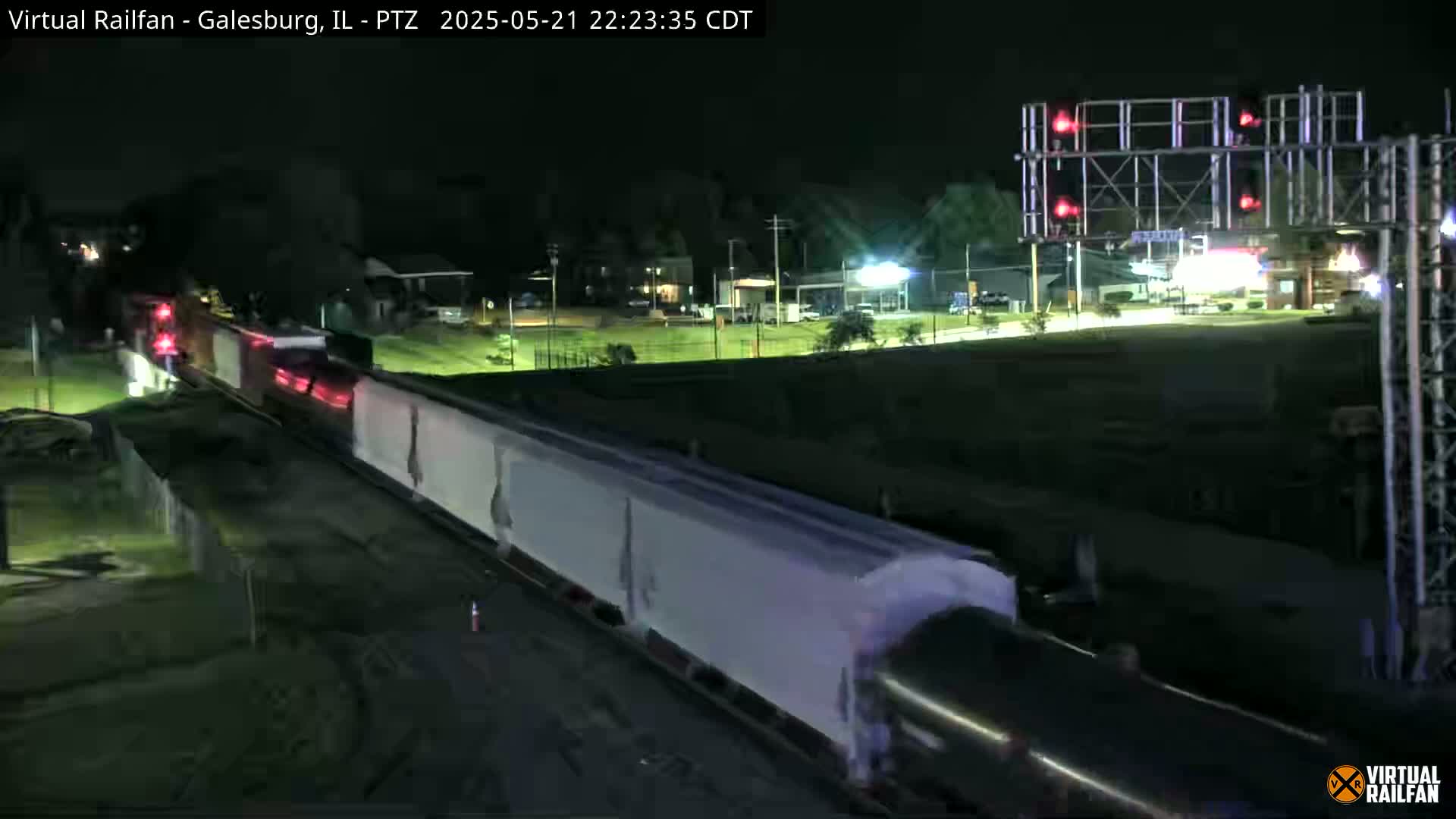 A long freight train passes under a nighttime sky near a lighted industrial area.