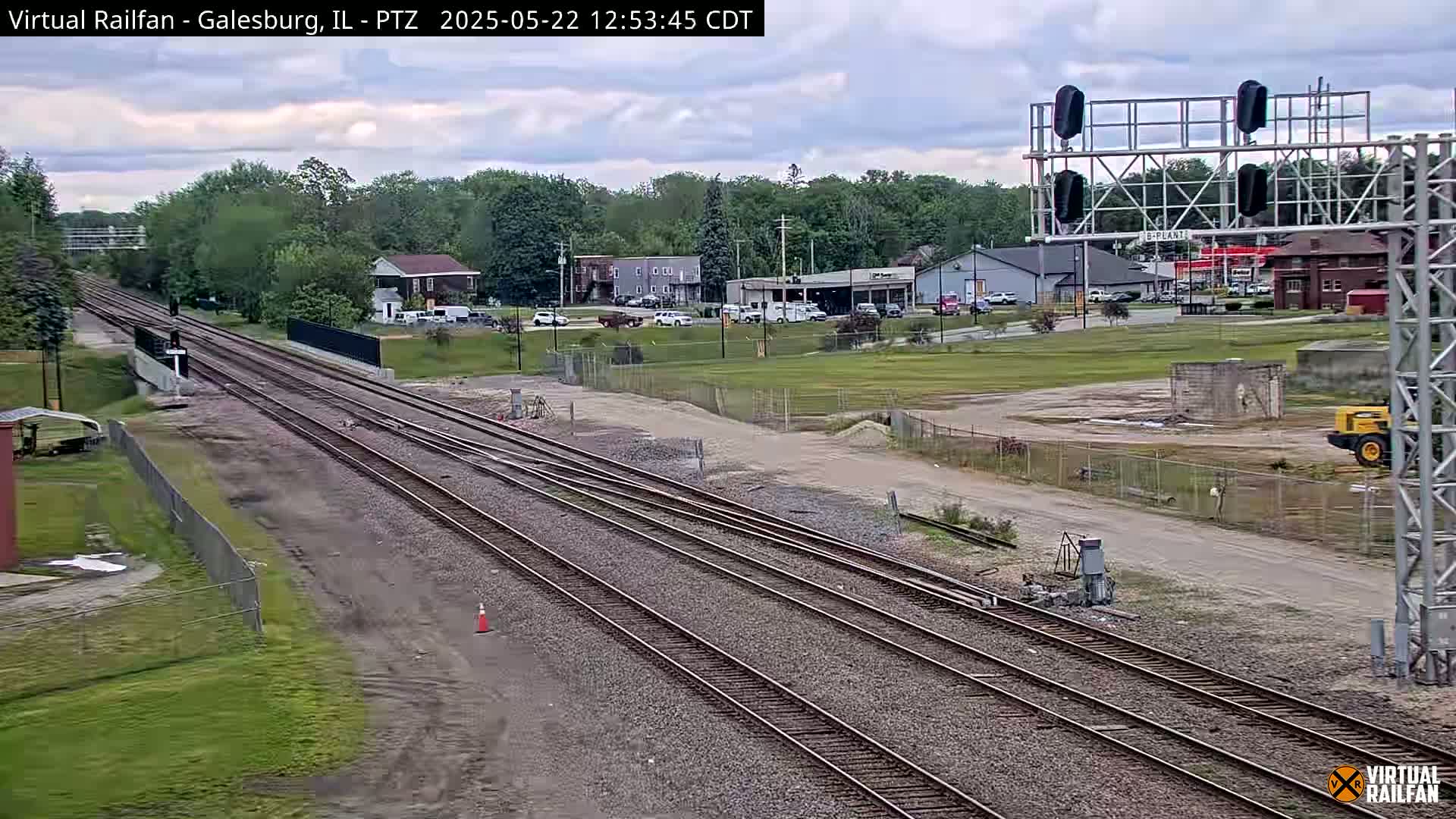 Multiple train tracks extend into the distance under a partly cloudy sky, passing by a small town with buildings and vehicles.