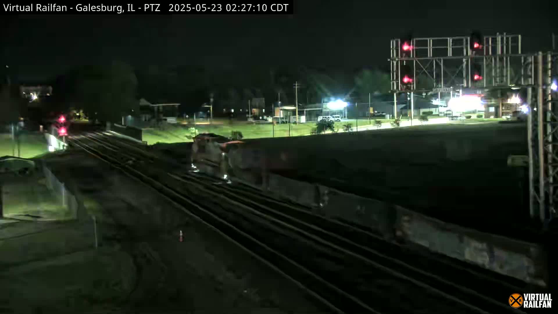 A long freight train passes under a railroad crossing signal at night.