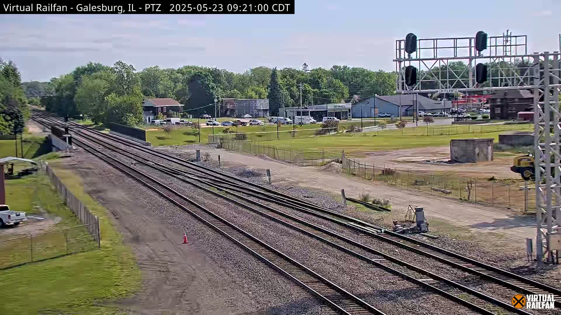Multiple sets of train tracks stretch into the distance under a clear sky, past a small town with buildings and vehicles.