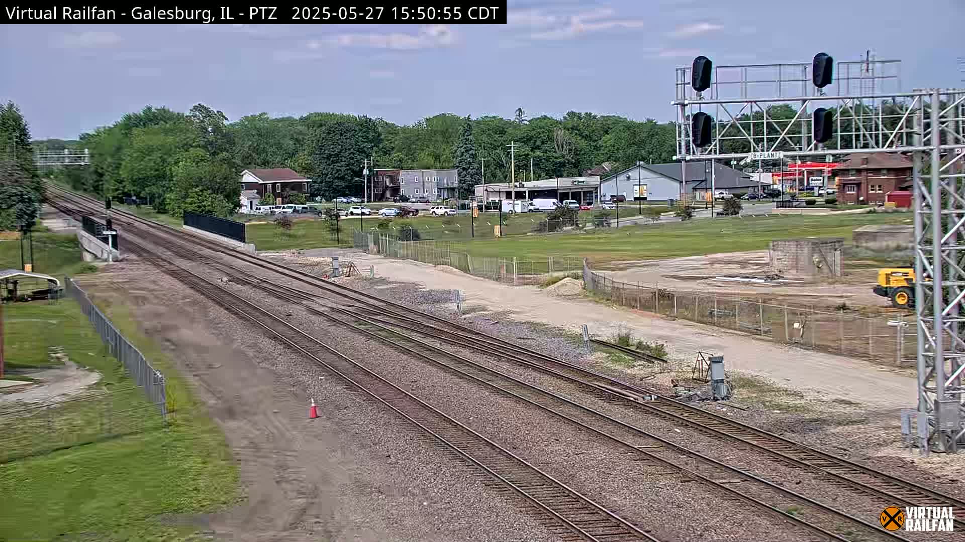 Multiple train tracks extend into the distance under a partly cloudy sky, past a construction site and buildings.