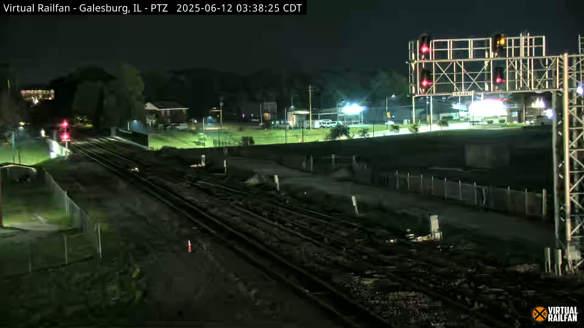 A nighttime view of railroad tracks undergoing construction or maintenance, with streetlights illuminating a nearby road and grassy area.