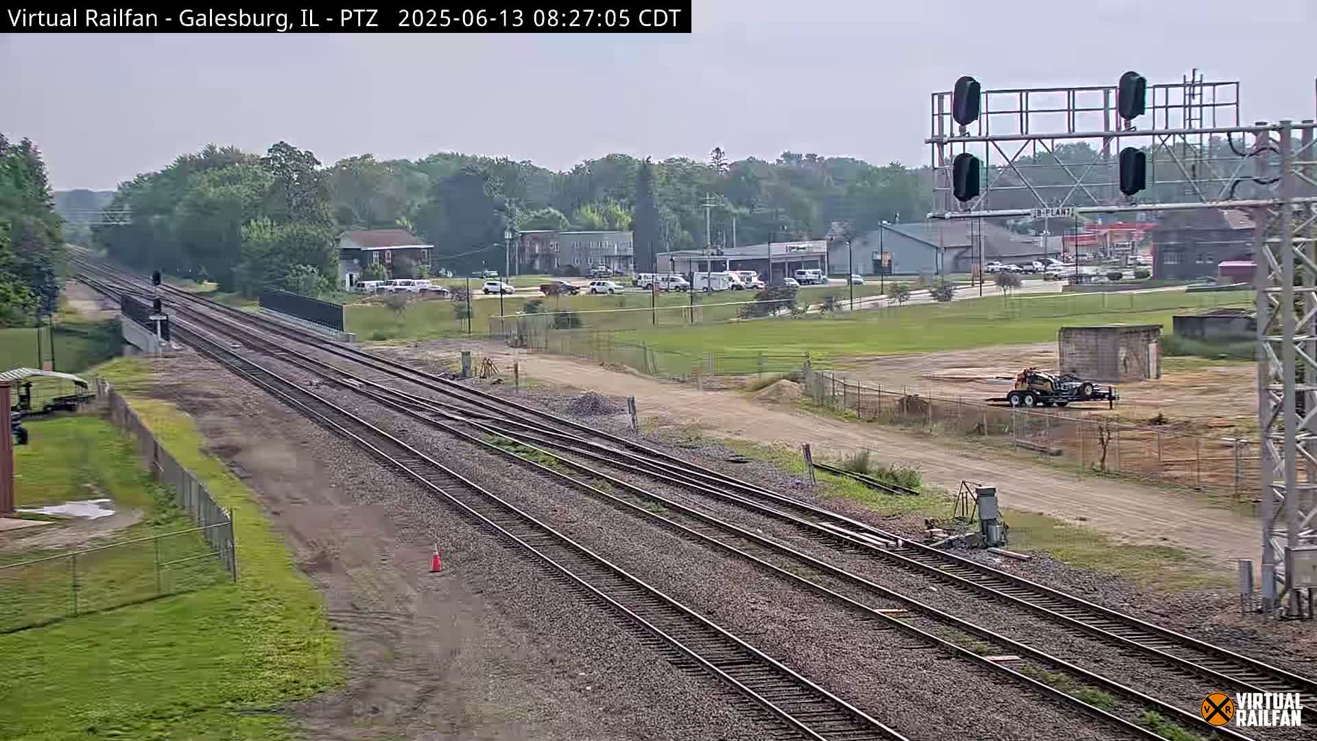 Multiple sets of train tracks extend into the distance under a partly cloudy sky, passing by a small town with some construction equipment visible nearby.