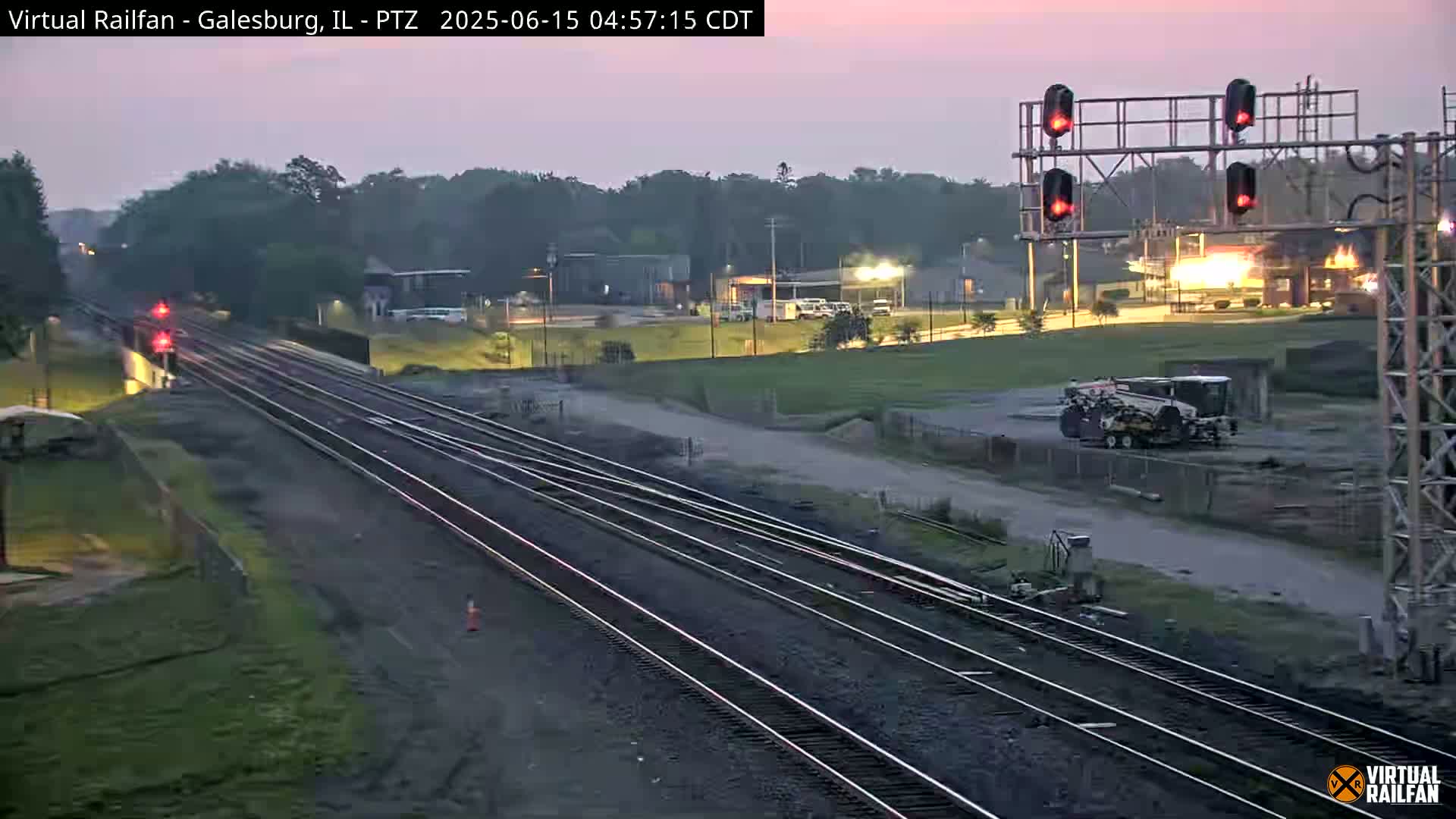 Multiple sets of railroad tracks extend into the distance under a twilight sky, with a piece of industrial machinery visible in the midground.