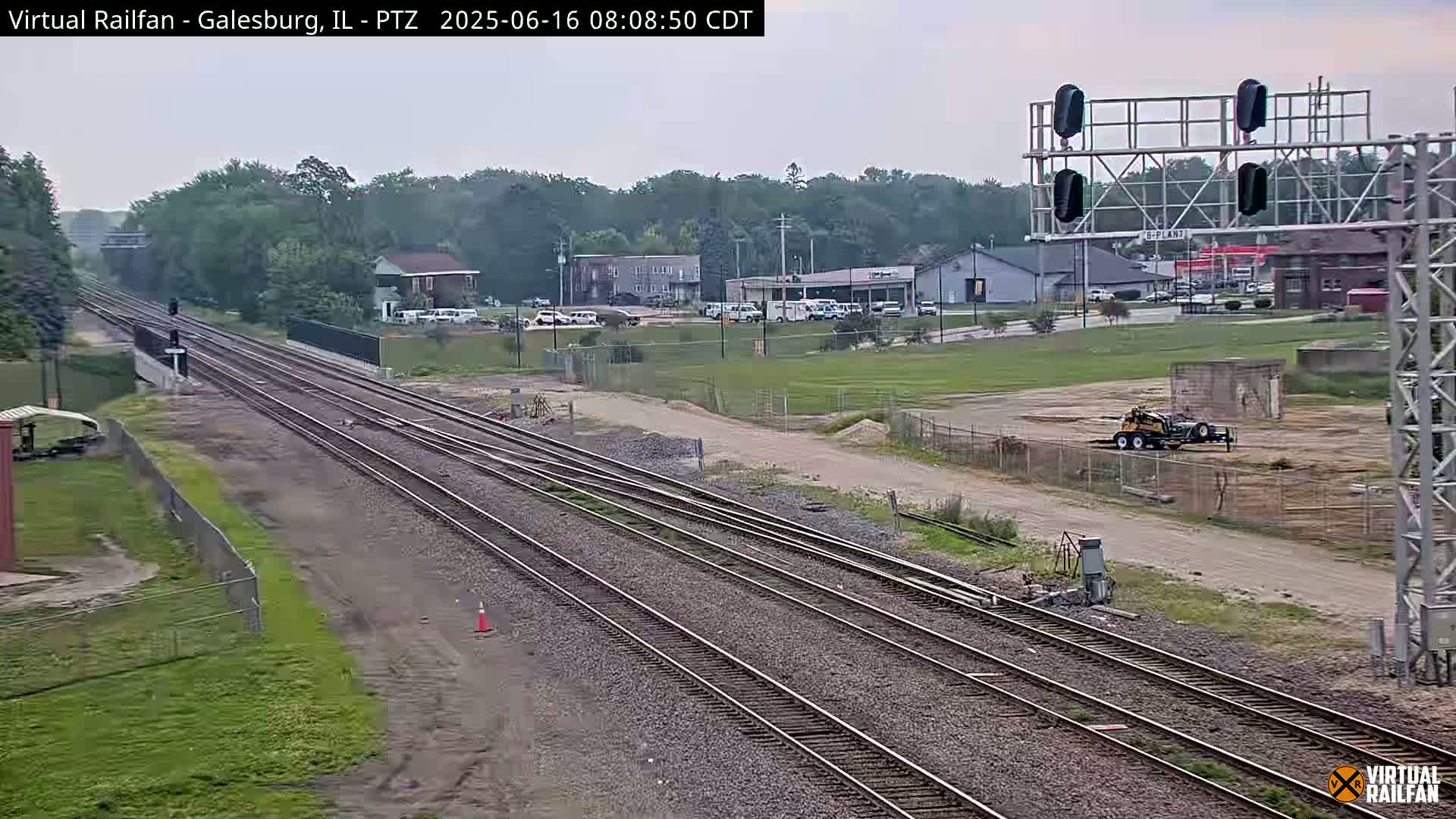 Multiple sets of train tracks extend into the distance under an overcast sky, passing through a landscape featuring some buildings and a construction site.