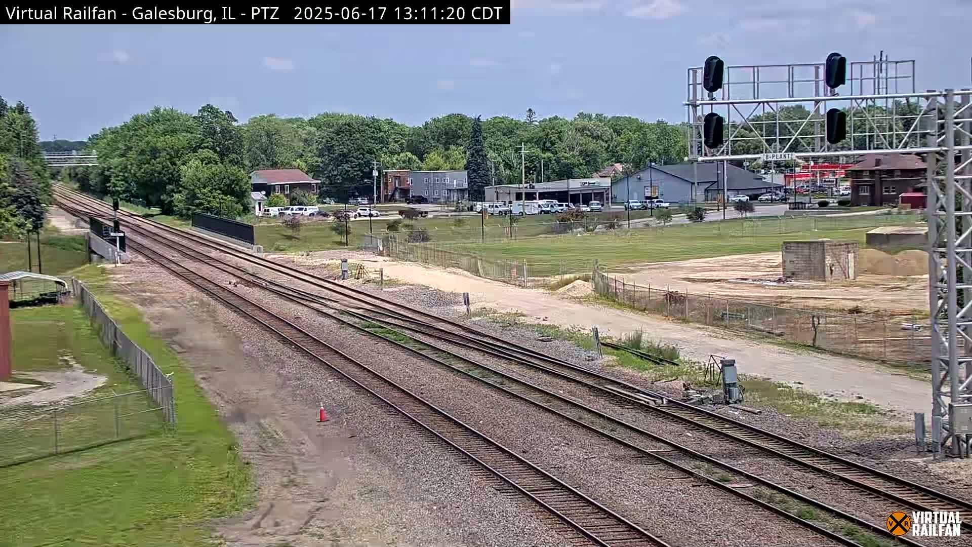 A long view of several parallel train tracks on a sunny day, extending into a distance where buildings and trees are visible.