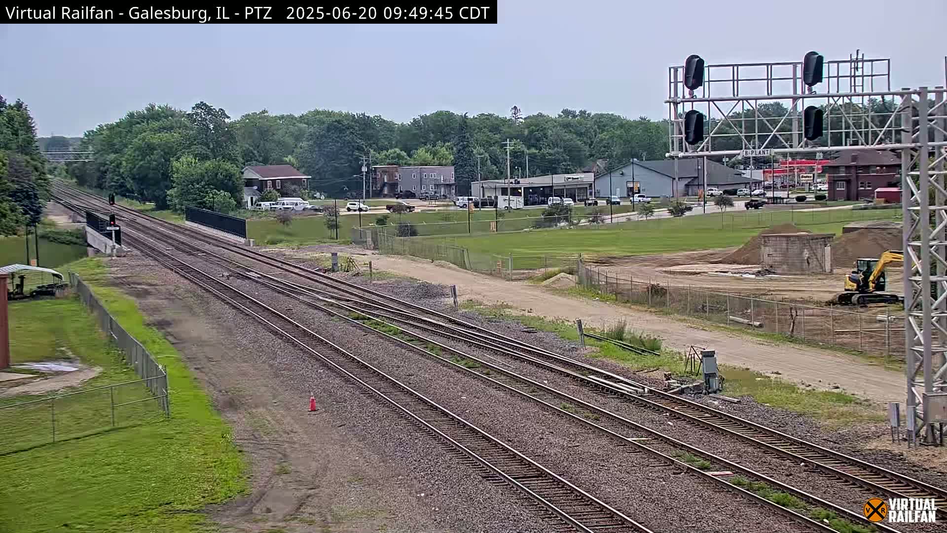 Multiple sets of train tracks stretch into the distance under a partly cloudy sky, passing by a small town with buildings and construction activity nearby.