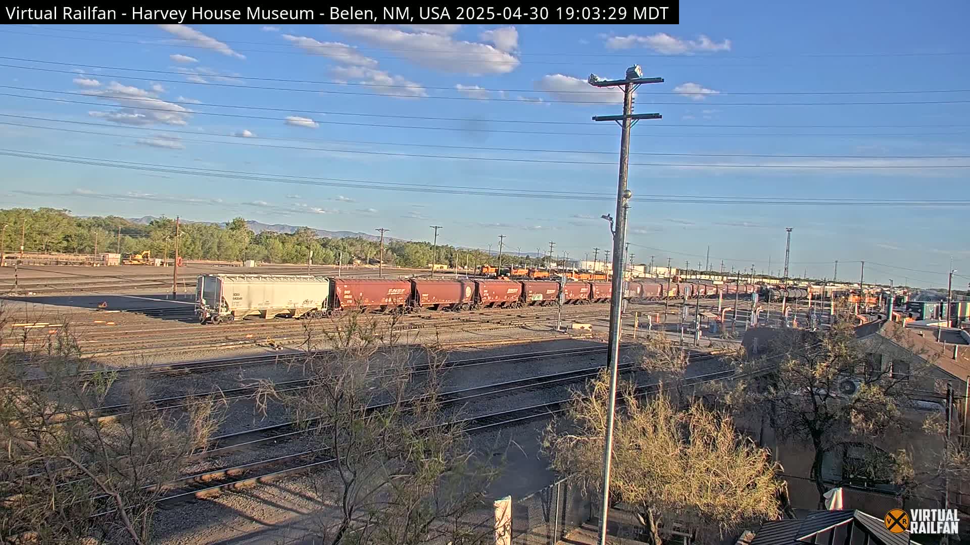 A long freight train sits on railroad tracks under a mostly clear, sunny sky.