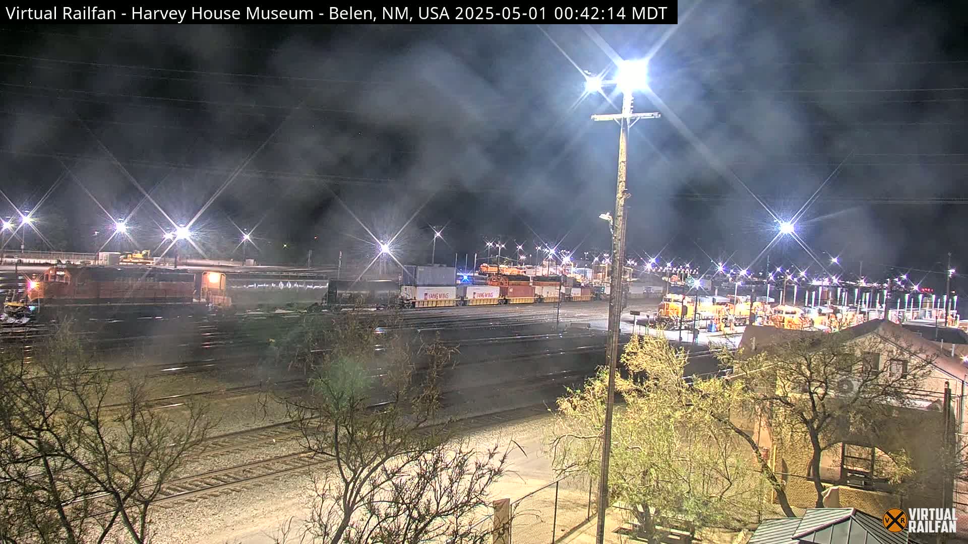 A nighttime view of a rail yard with multiple train cars and locomotives under hazy conditions.