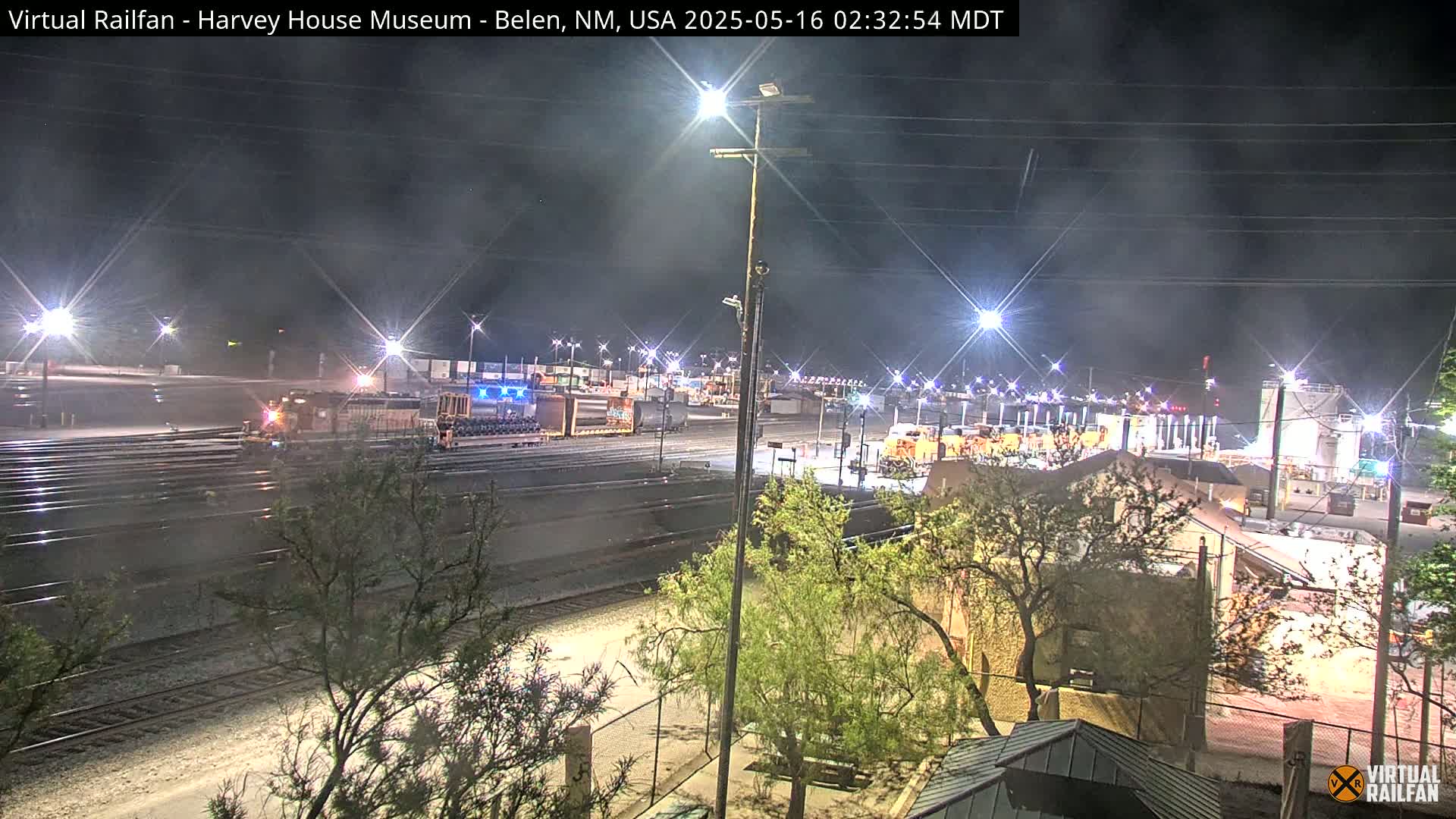 A nighttime view of a train yard with a locomotive and freight cars under hazy conditions.