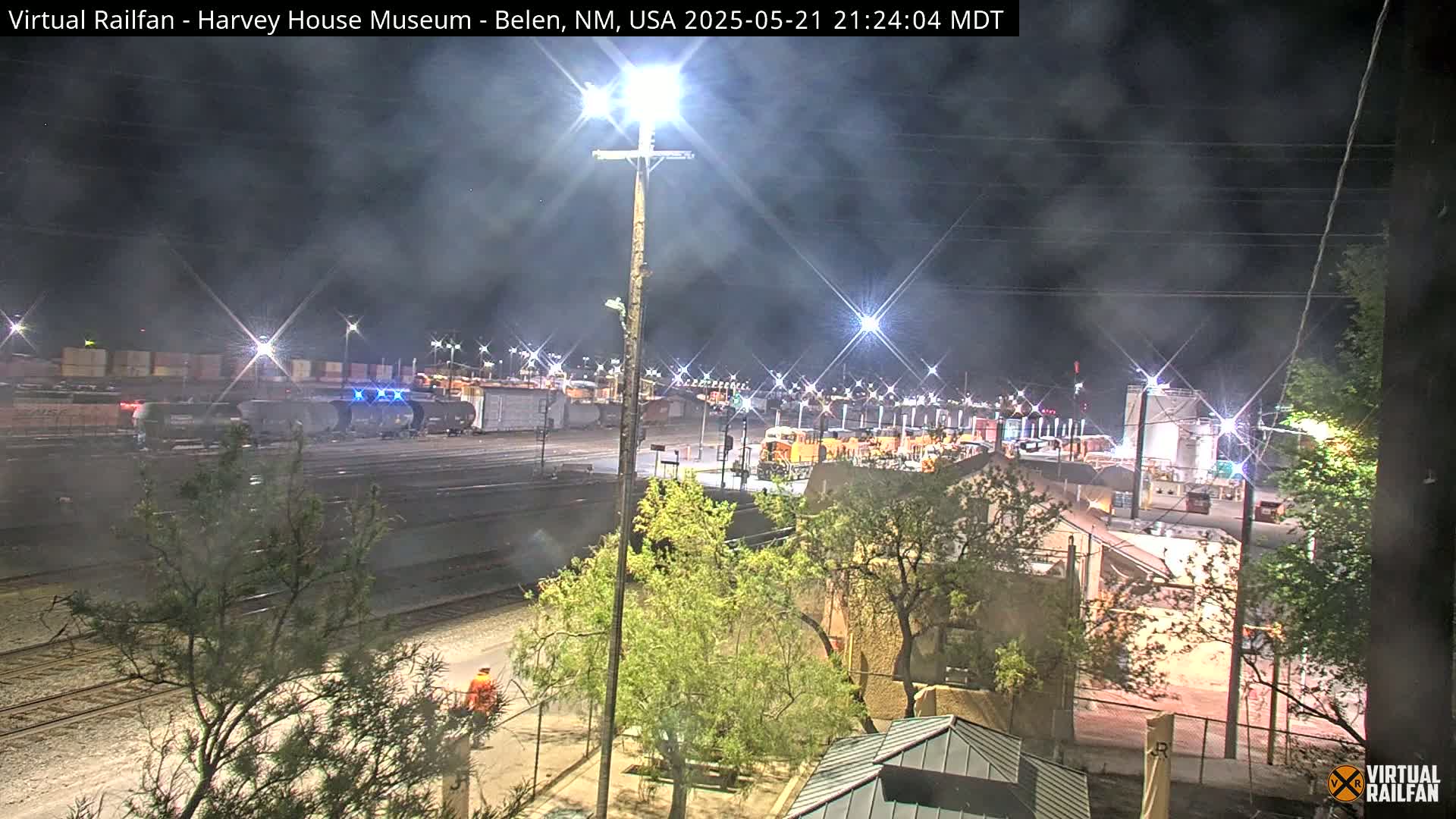 A nighttime view of a rail yard with several train cars and locomotives under a hazy, dark sky.