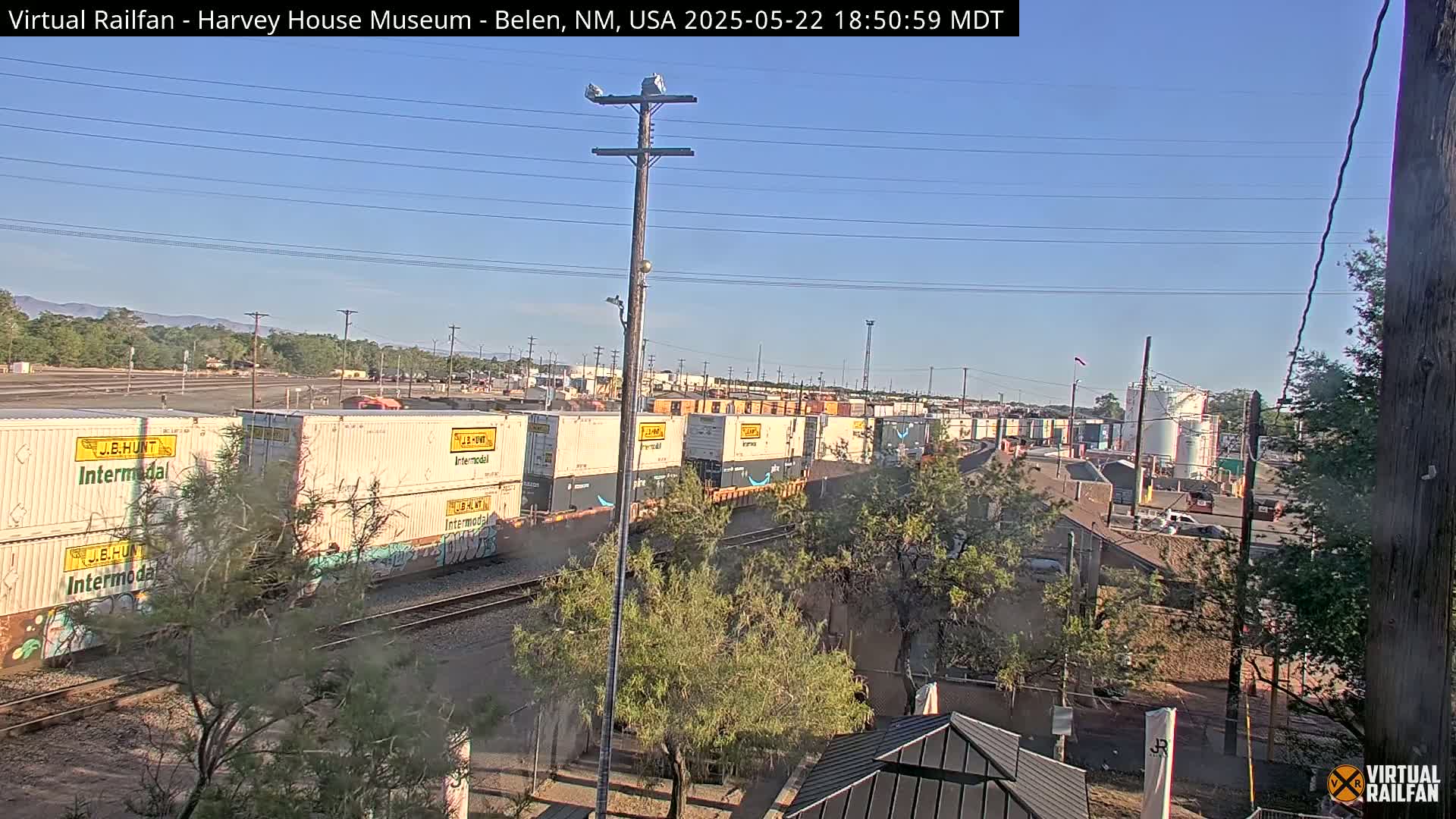 A long freight train with multiple shipping containers sits on railroad tracks under a clear, sunny sky.