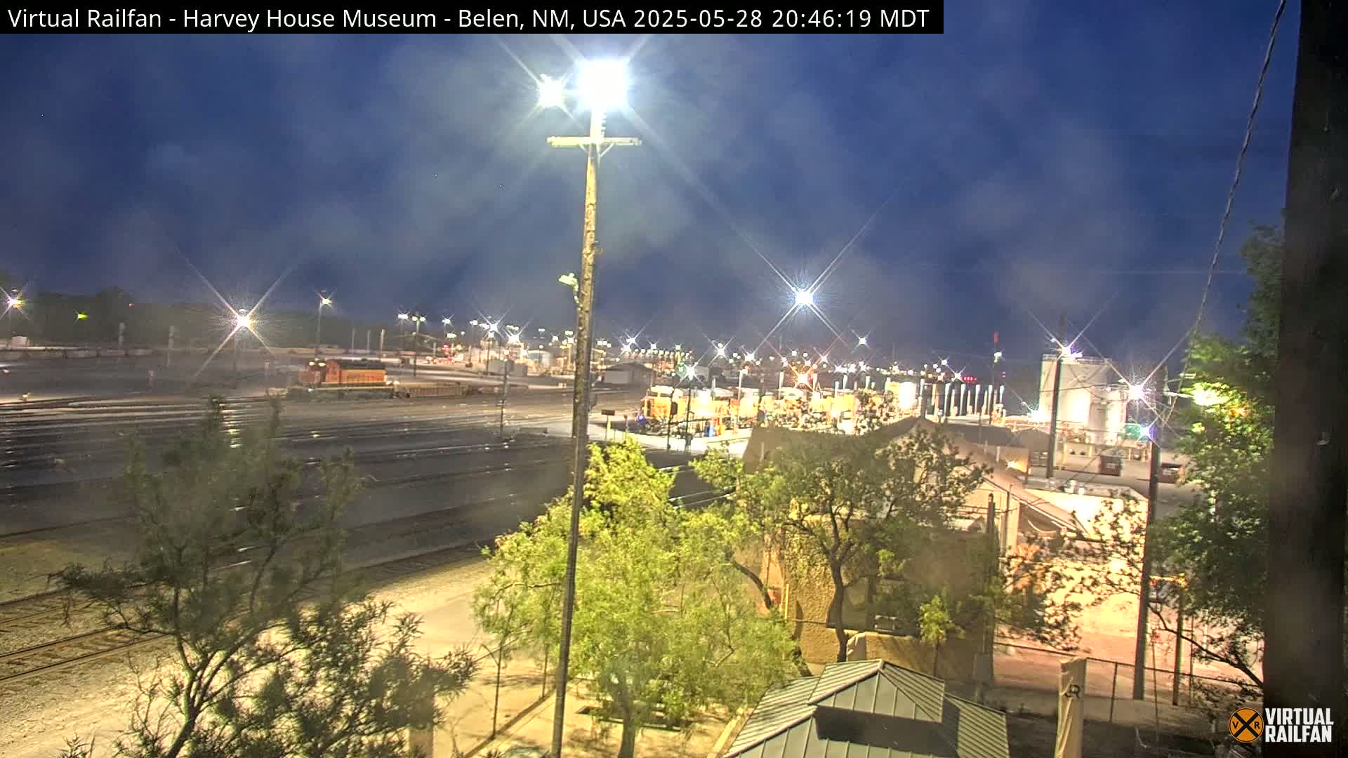 A nighttime view of a rail yard with a train and surrounding buildings under a twilight sky.