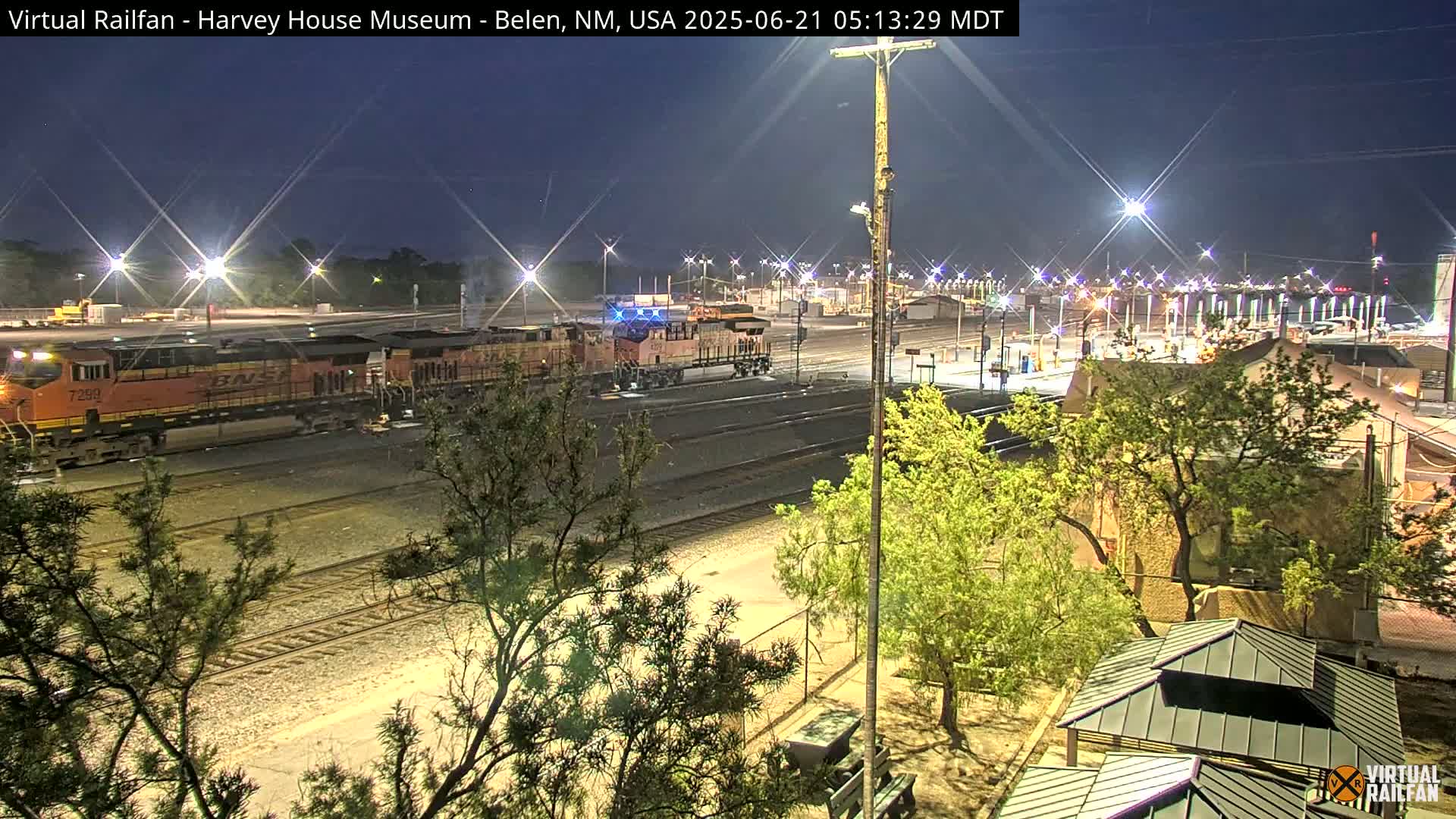 A nighttime view of a train yard with an orange locomotive and several rail cars under a clear, dark sky.