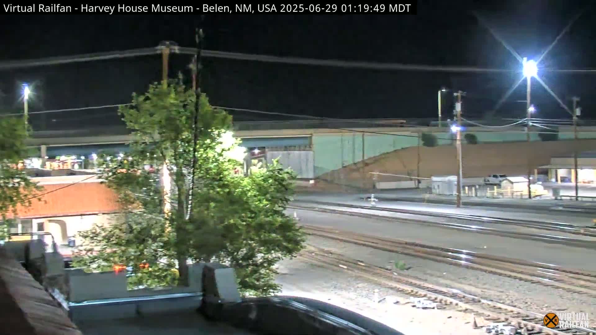 A nighttime view of train tracks, buildings, and trees under bright lights.