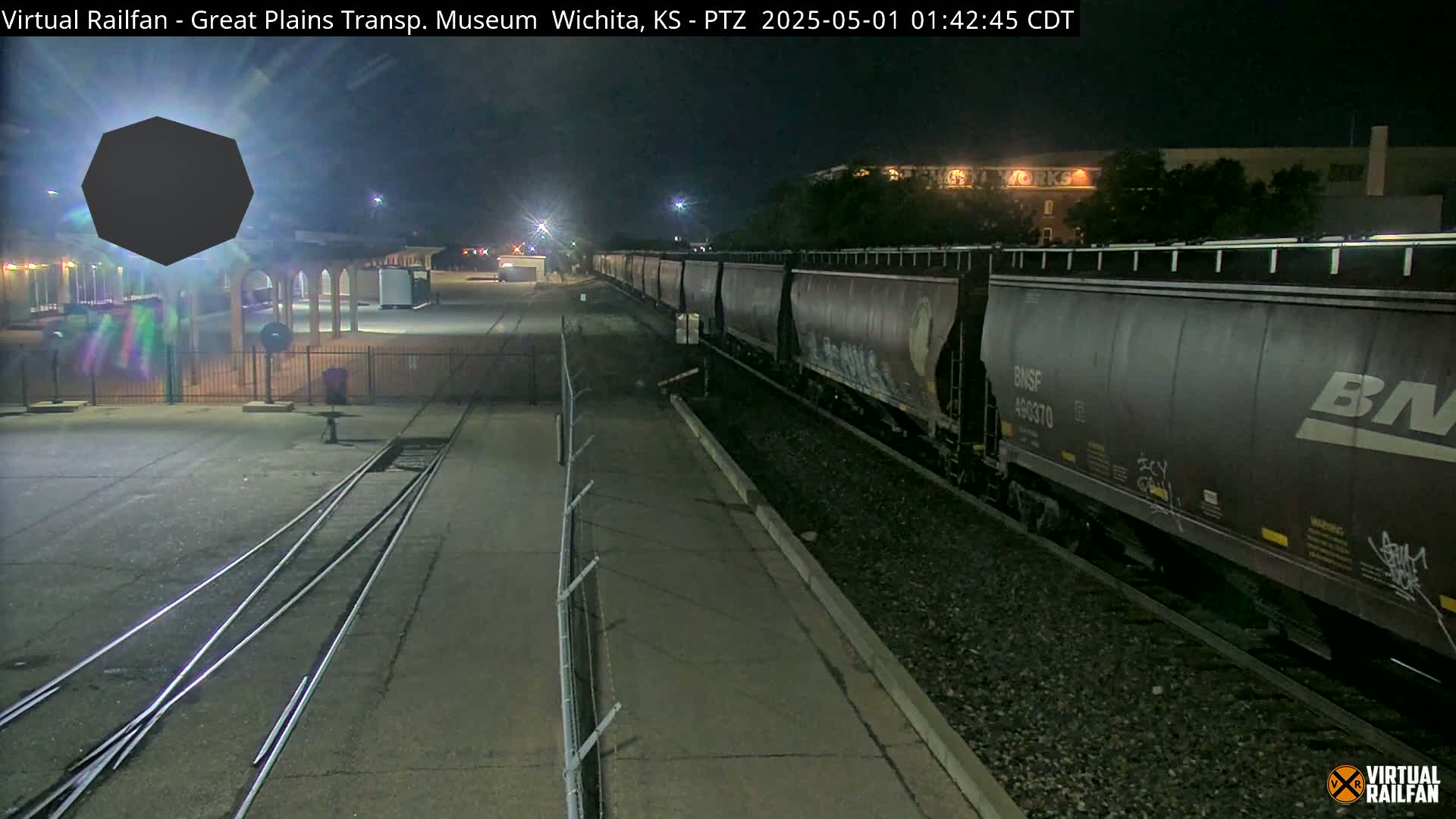 A long freight train passes by a rail yard at night.