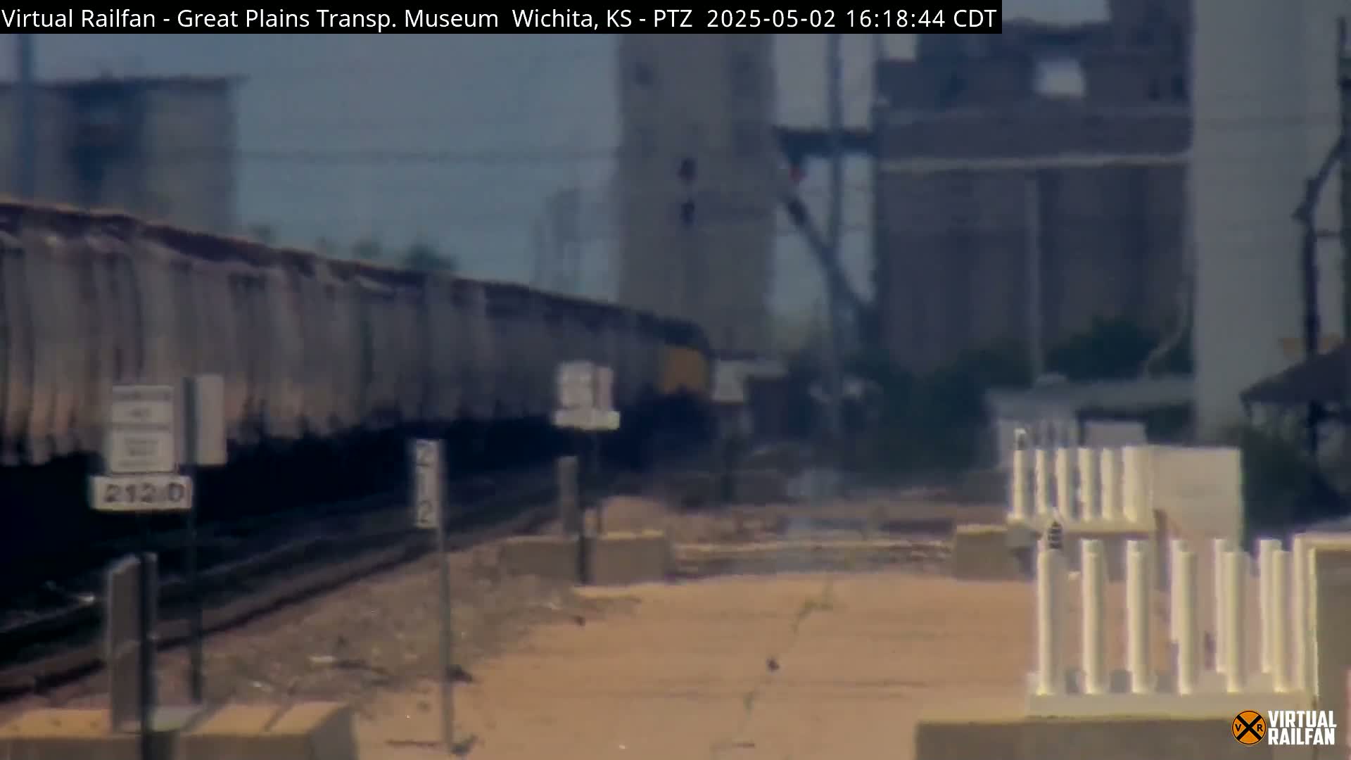 A long freight train is passing by an industrial area on a hazy day.