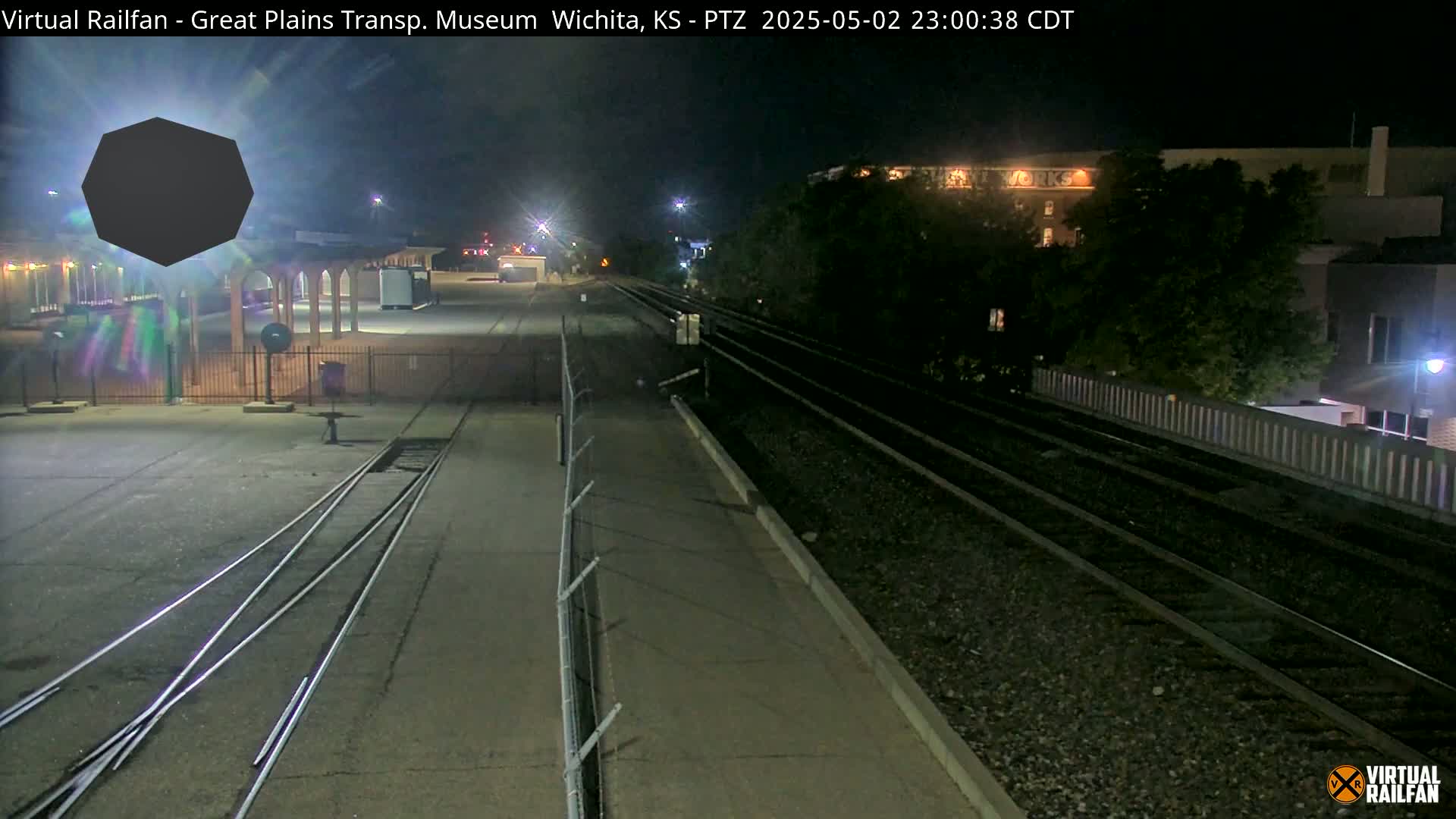 A nighttime view of railroad tracks near a building, with a dark, polygon-shaped object in the foreground.