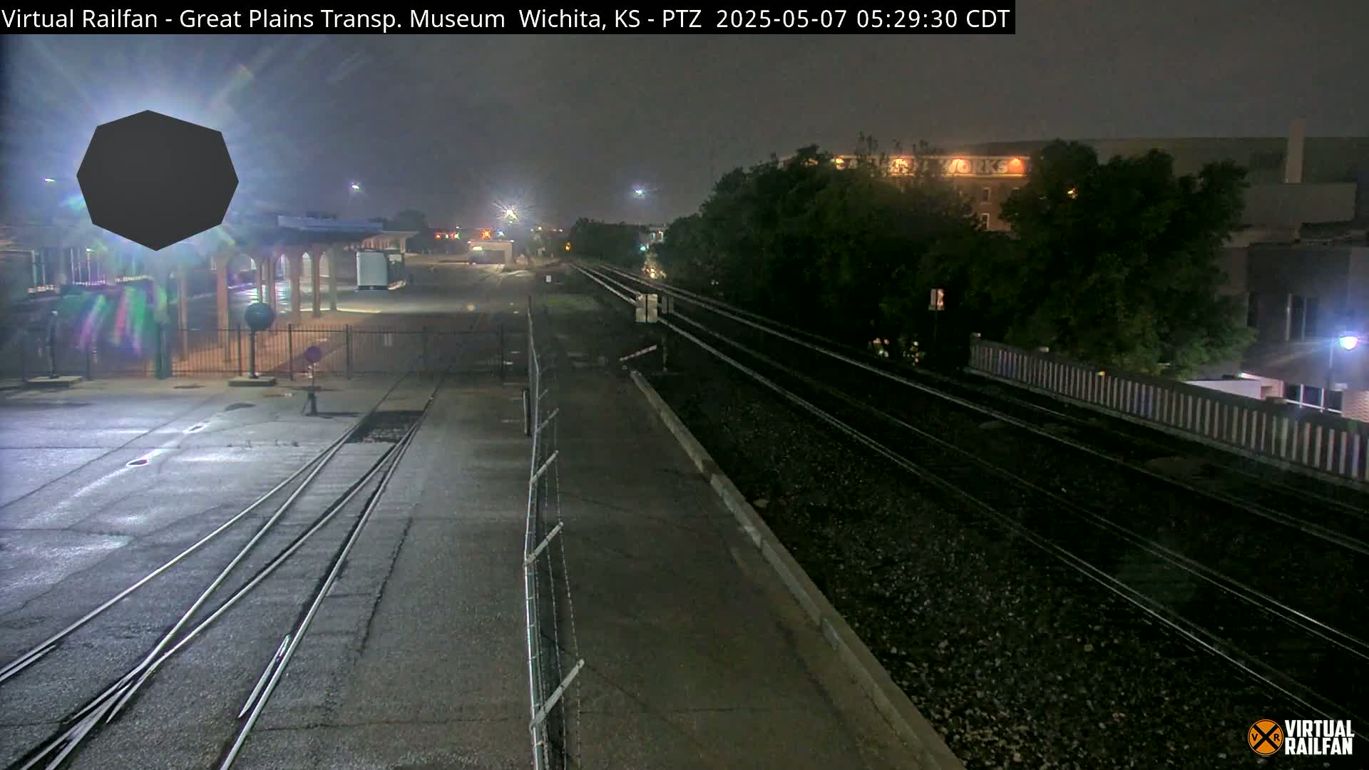 A nighttime view of railroad tracks and a railway station, partially obscured by shadows and darkness.