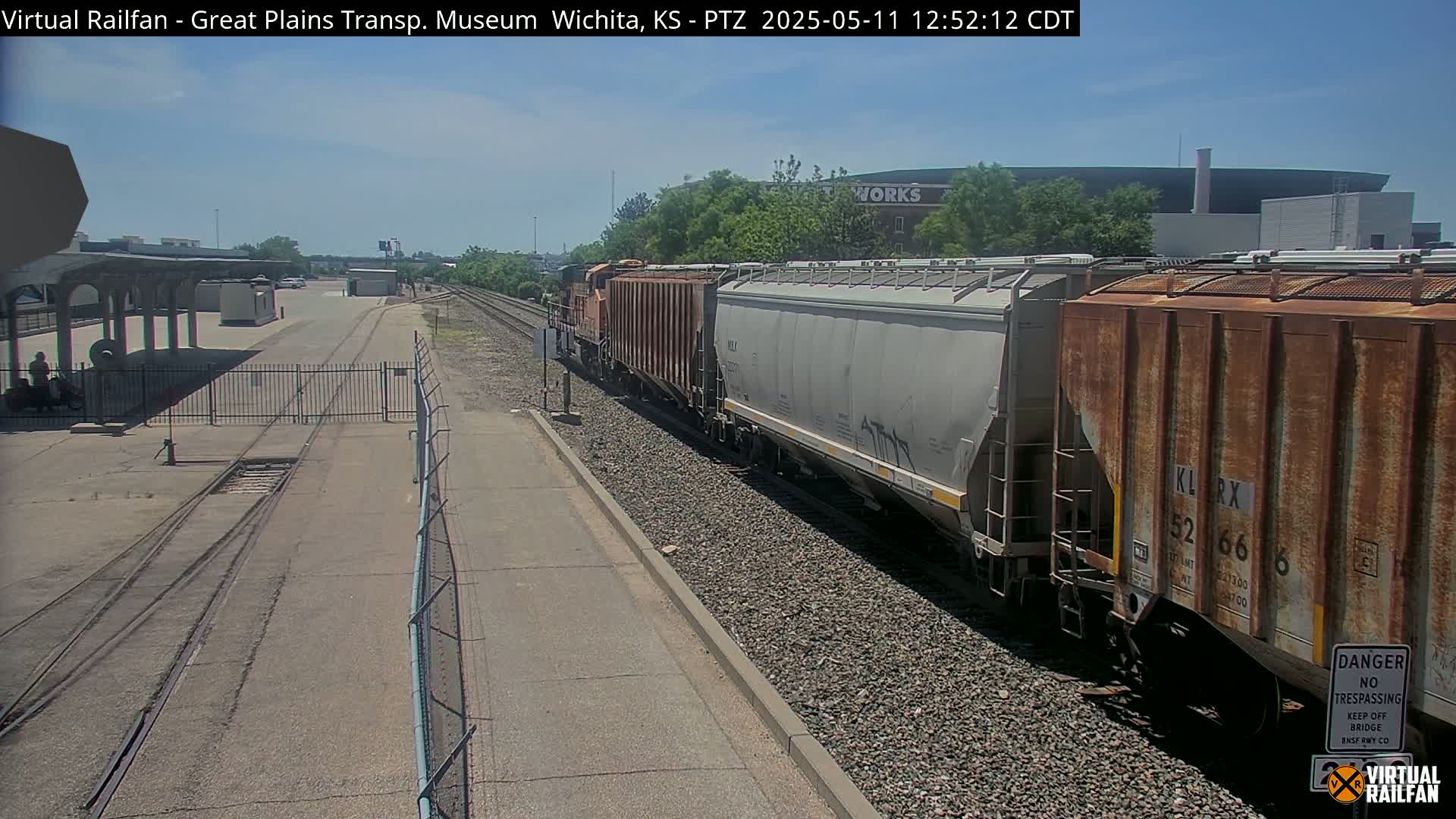 A freight train passes by a railway station on a sunny day.