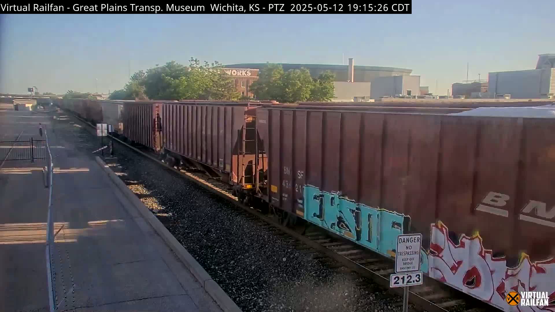 A long freight train with graffiti on some cars moves along railroad tracks under a clear, sunny sky.