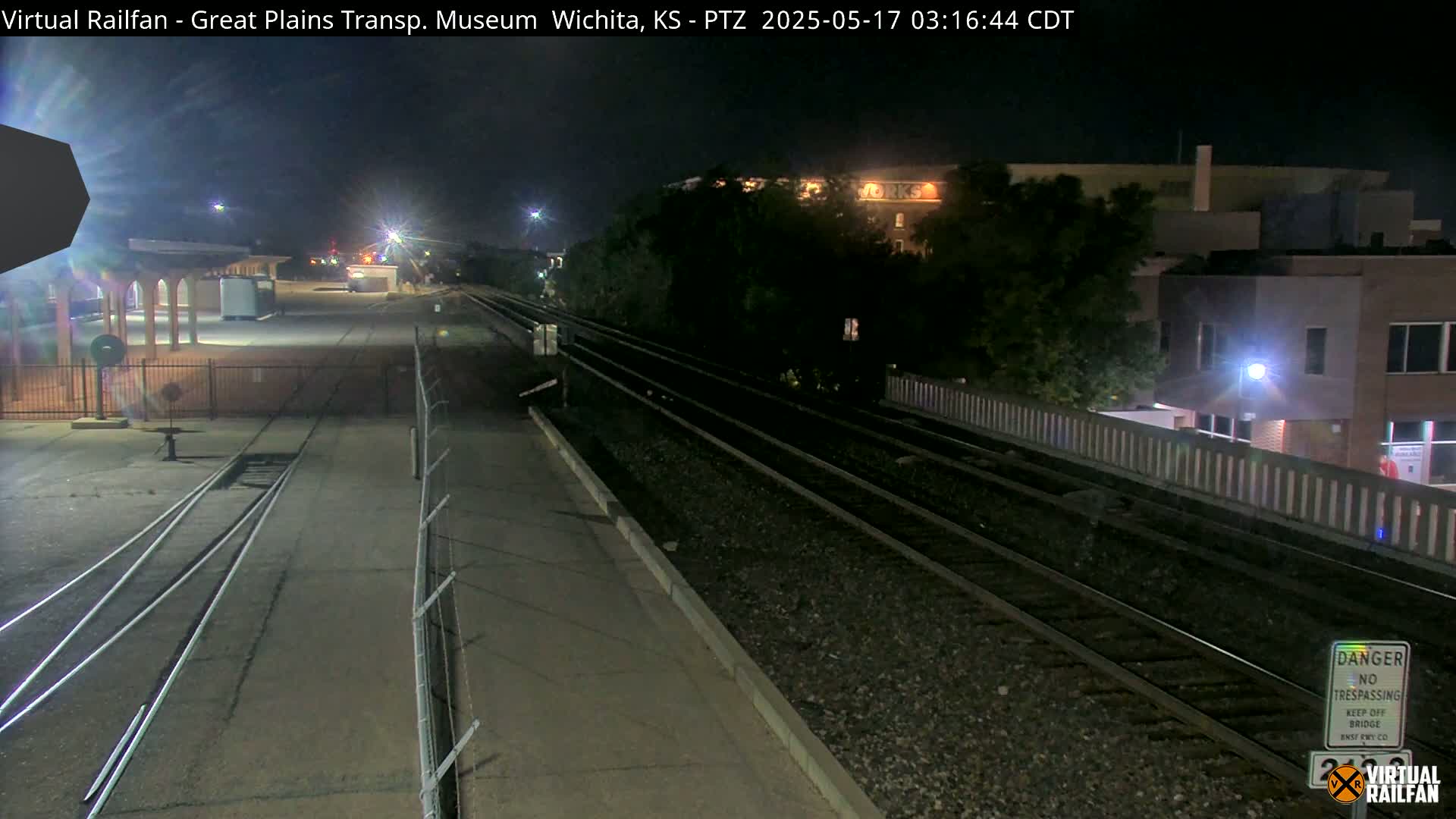 A nighttime view of train tracks extending from a station platform toward buildings under a clear sky.
