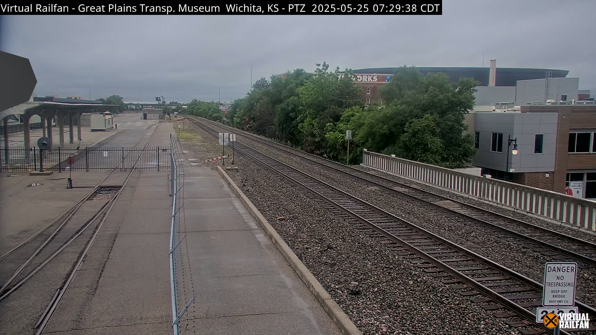 A view of train tracks, a railway station platform, and surrounding buildings on an overcast day.