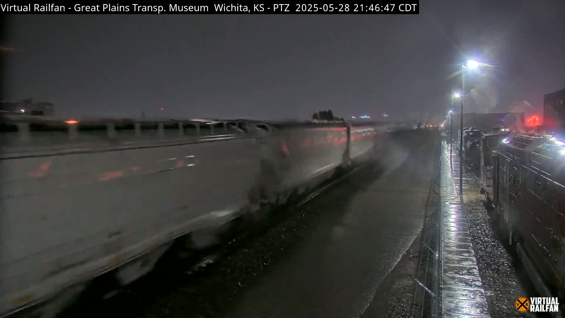 A long freight train and a smaller train pass each other on a wet, dark night under streetlights.