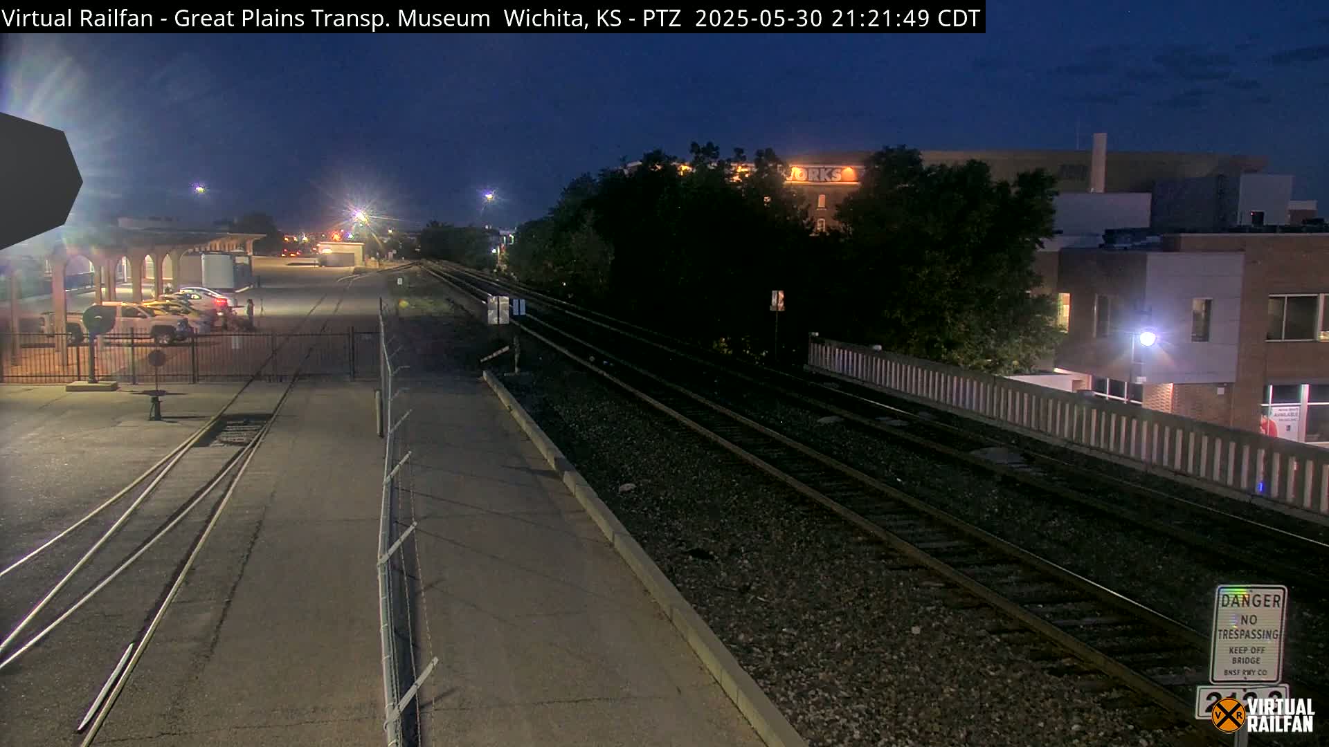 A nighttime view of train tracks and a parking lot with several cars, under a clear, dark sky.