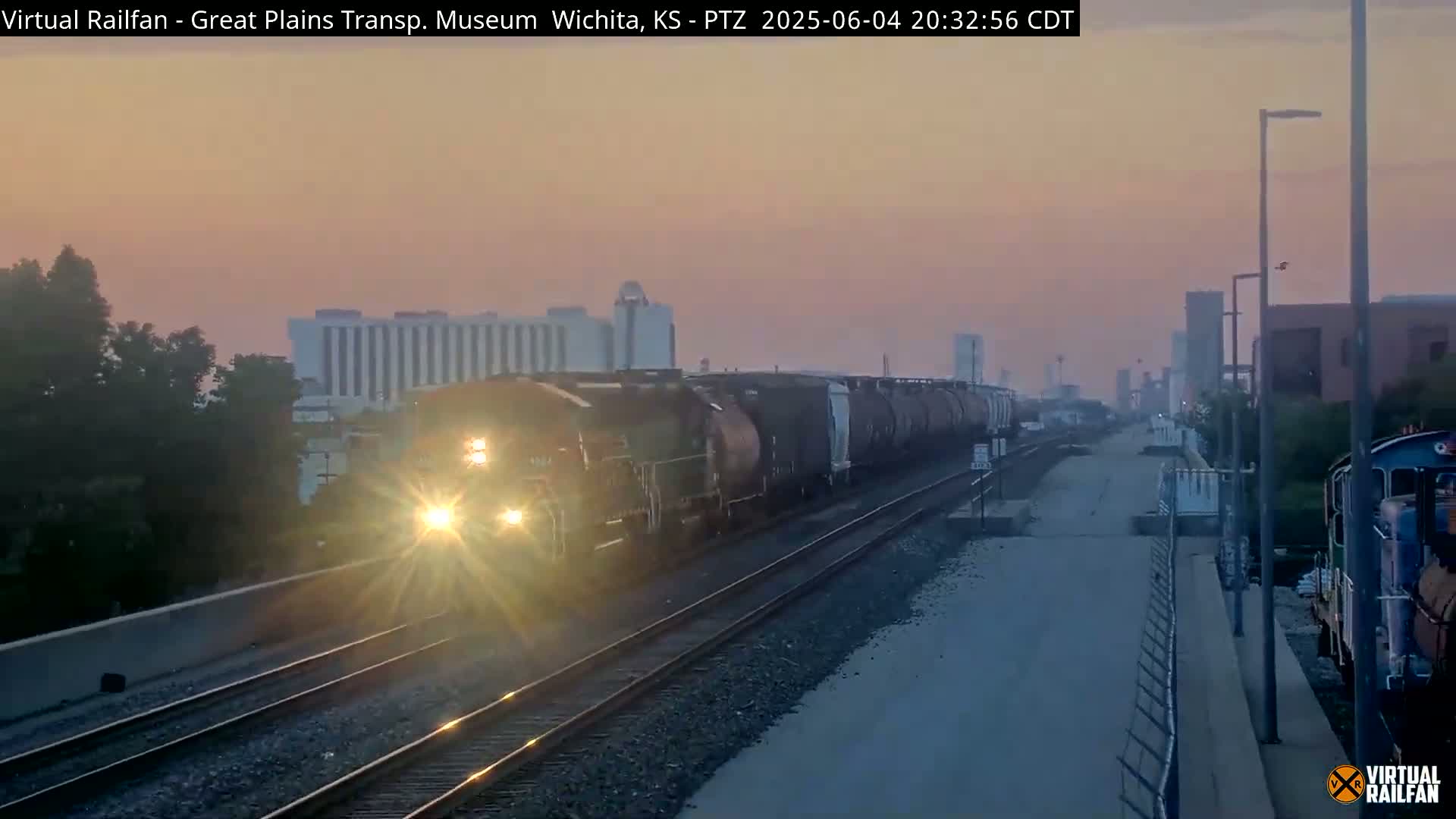 A long freight train passes by under a dusky pink and orange sunset.