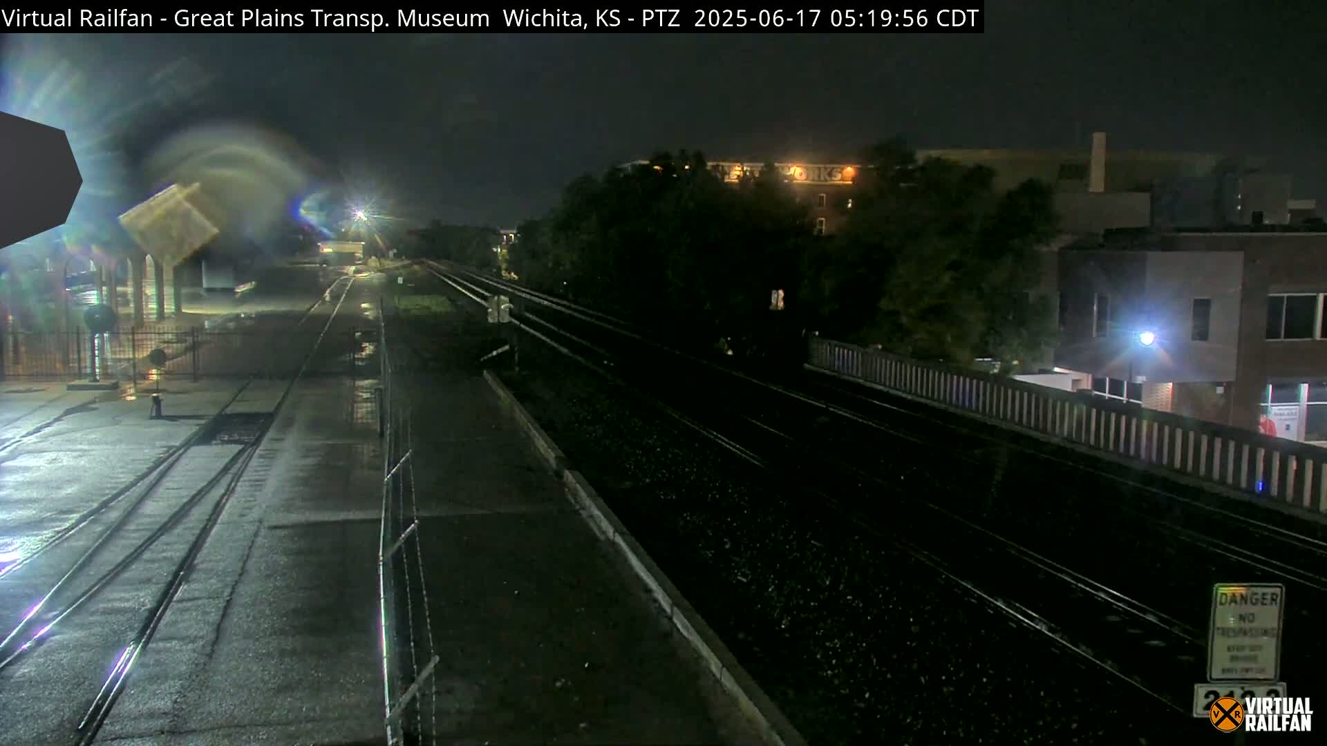 A nighttime view of rain-slicked train tracks and a nearby building under a dark sky.