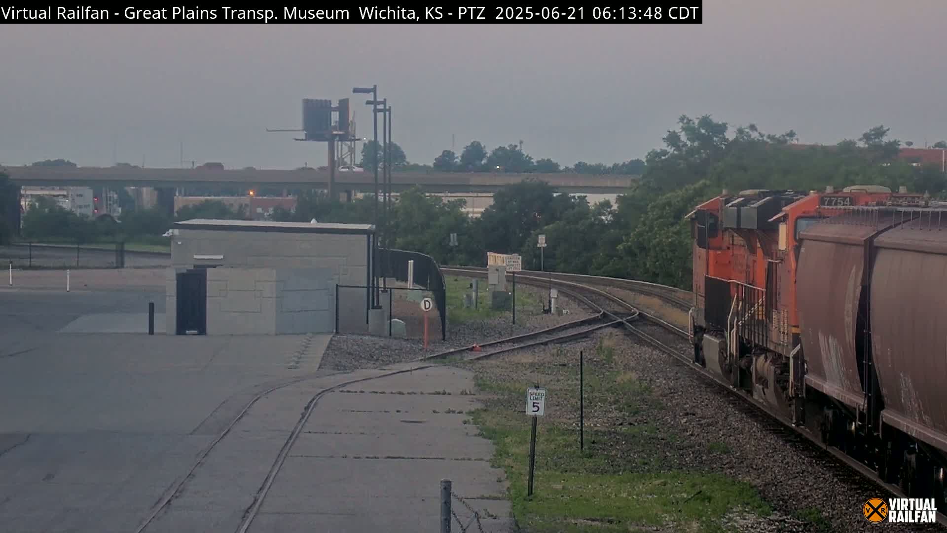 An orange locomotive pulling a freight train passes a railway junction under an overcast sky.