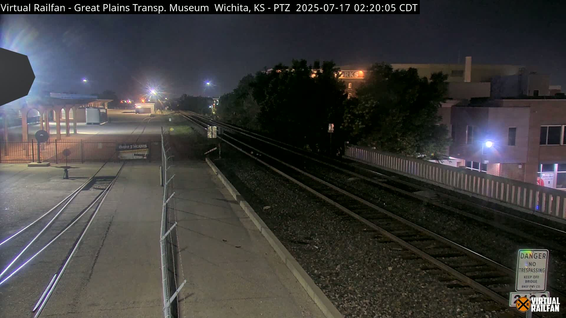 A nighttime view of railroad tracks extending into the distance, passing by a building and a partially visible station under a clear, dark sky.