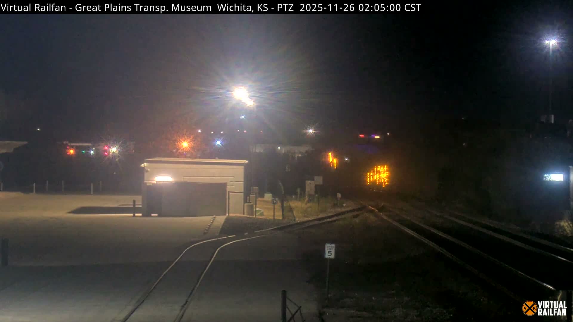 The image shows a clear, dark night over a railway yard with multiple tracks, a small building, and various bright lights illuminating the scene.