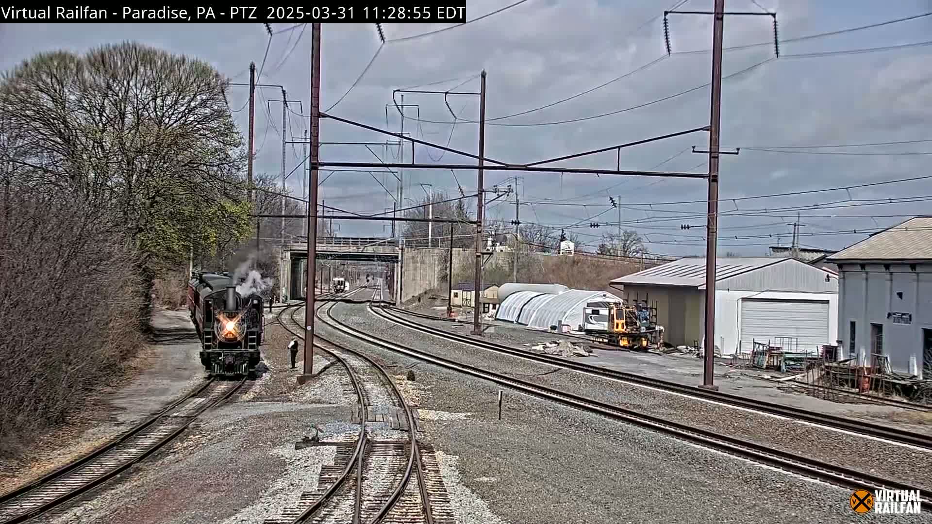 A steam locomotive is approaching a railway junction under a partly cloudy sky.