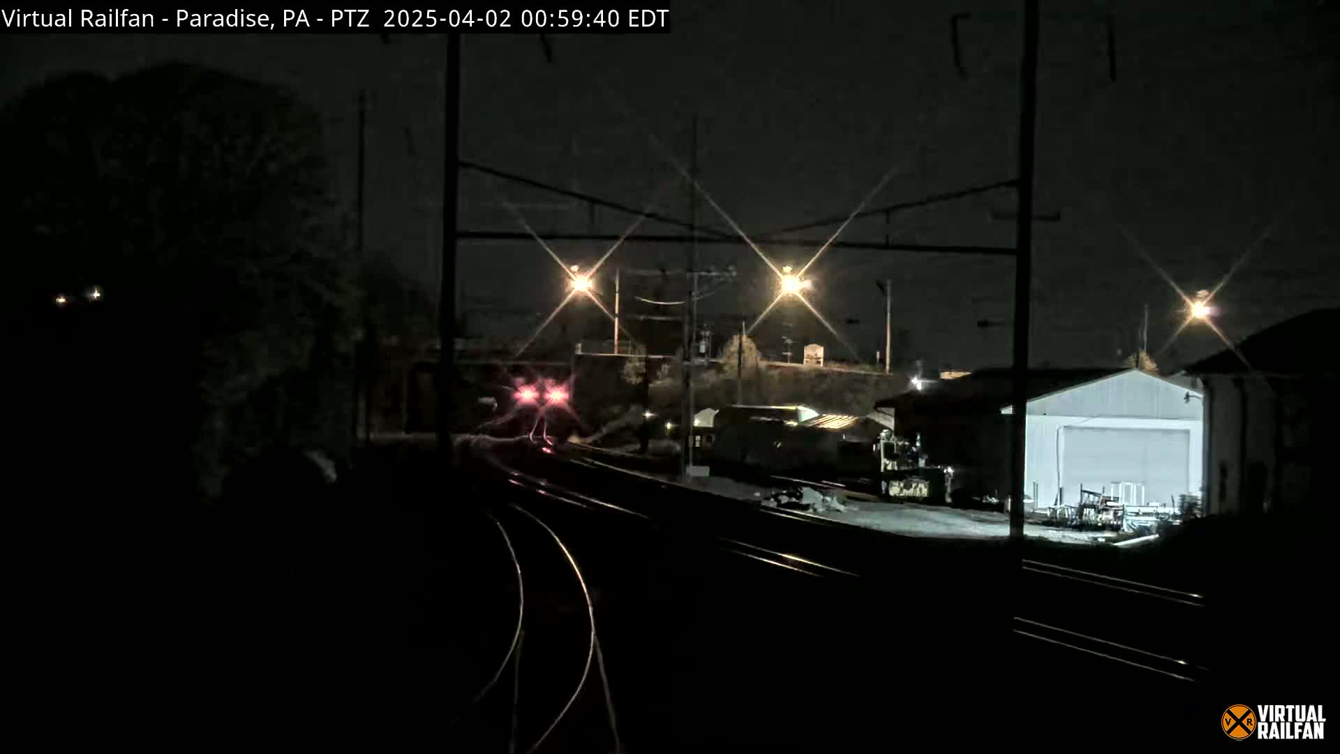 A nighttime view of a train passing by railroad tracks near a building, under artificial light.