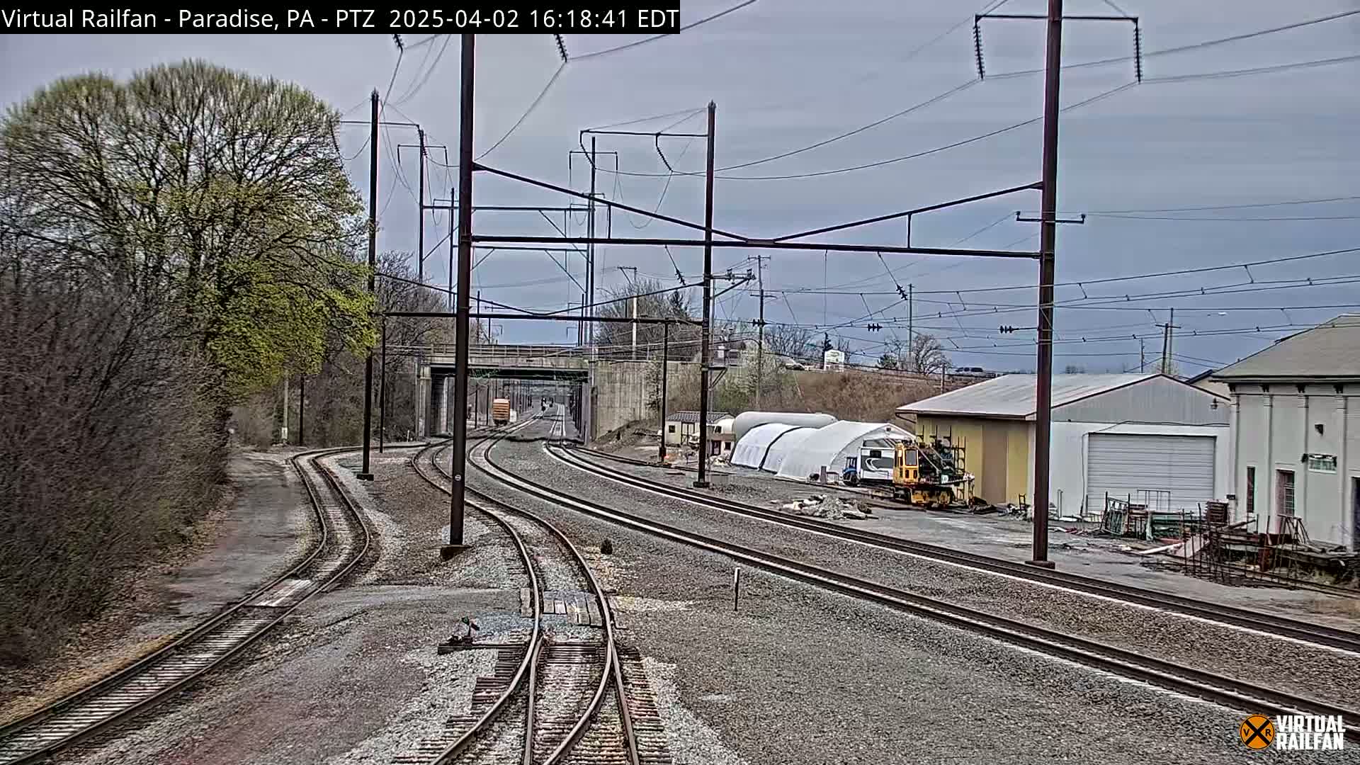 Multiple train tracks converge near some buildings under an overcast sky.