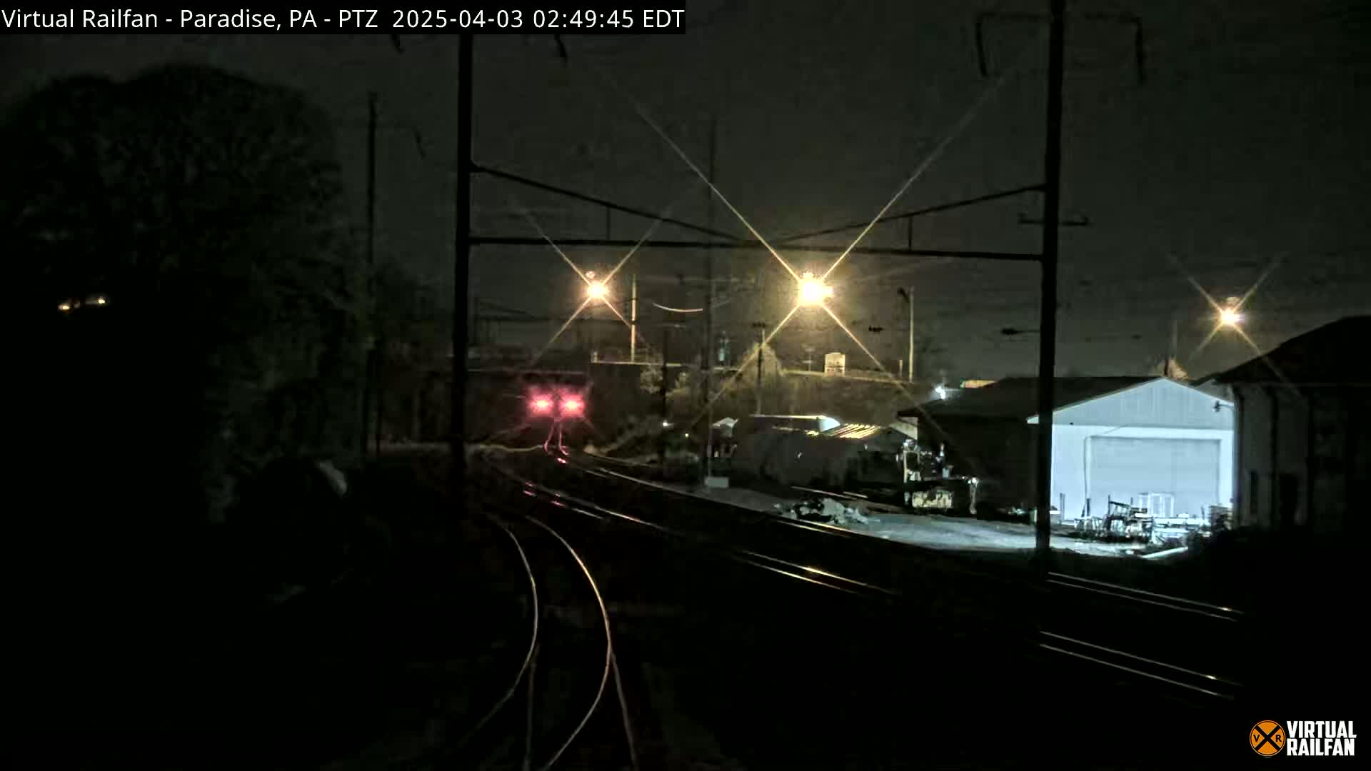 A train approaches a rail yard at night, under bright artificial lights.